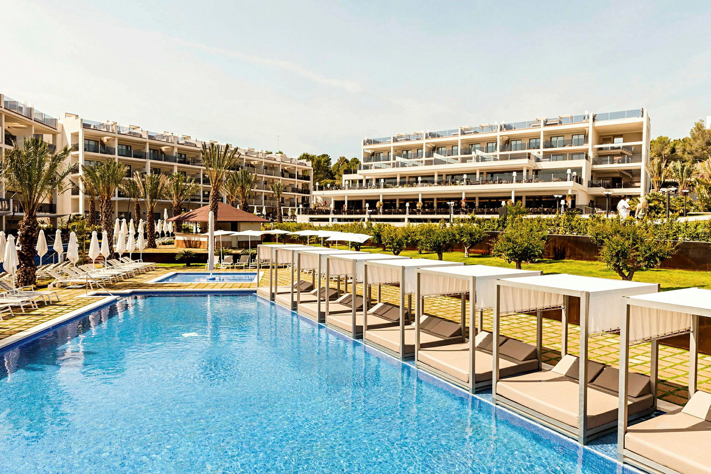 Hotellområde med pool, solstolar och byggnad i bakgrunden. (AI-genererad text)