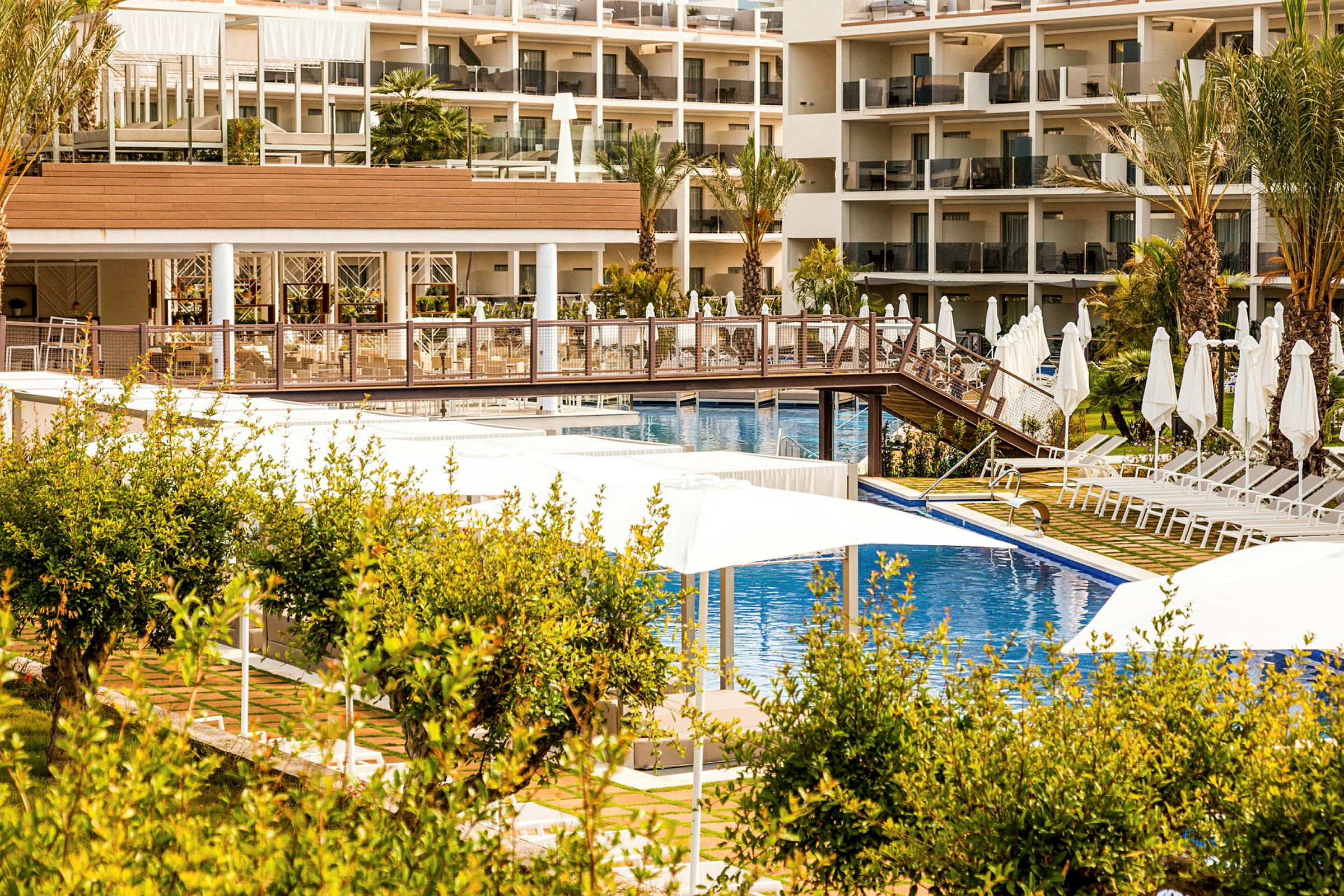 Hotellområde med pool, solstolar och parasoll utomhus, omgiven av grönska. (AI-genererad text)