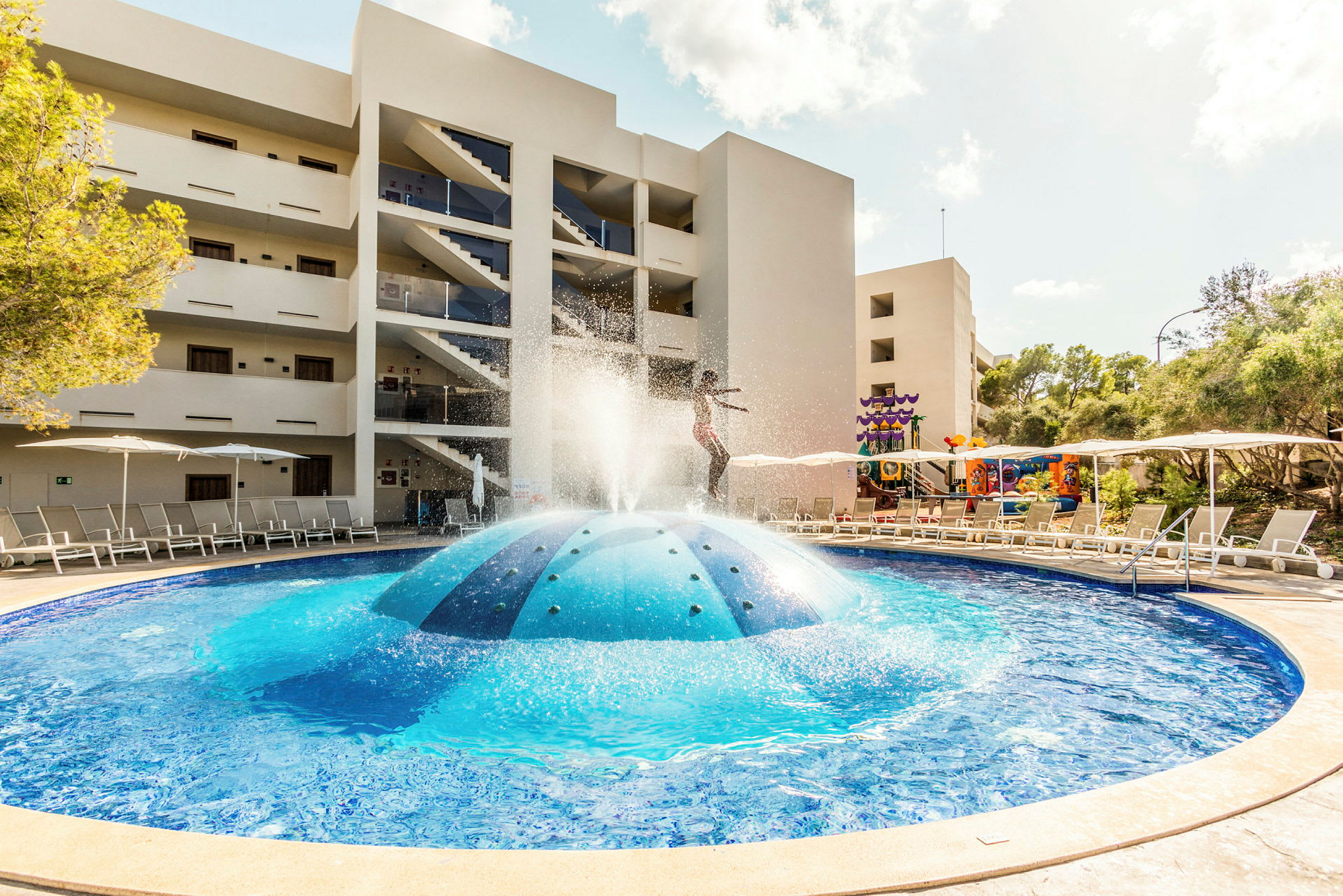 Utomhuspool med fontän nära hotellbyggnad. (AI-genererad text)