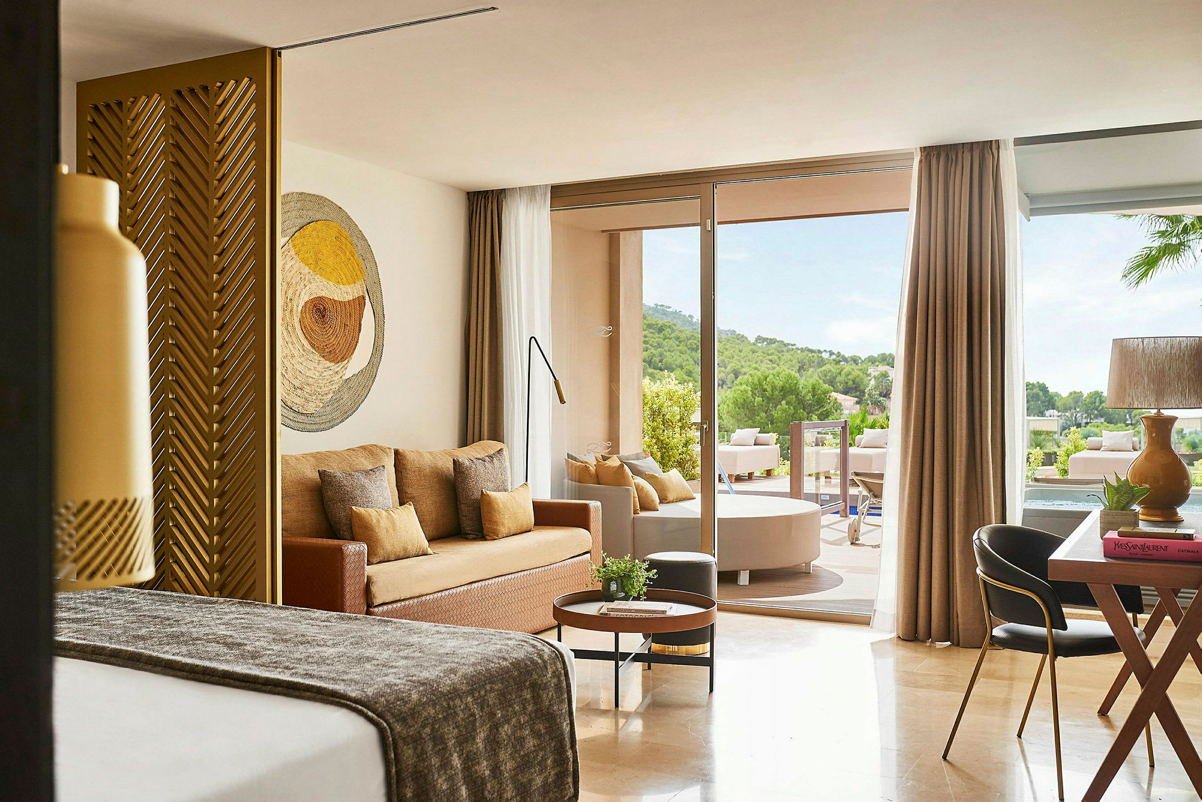Ett modernt hotellrum med sittgrupp och en uteplats med utsikt över grönska. (AI-genererad text)