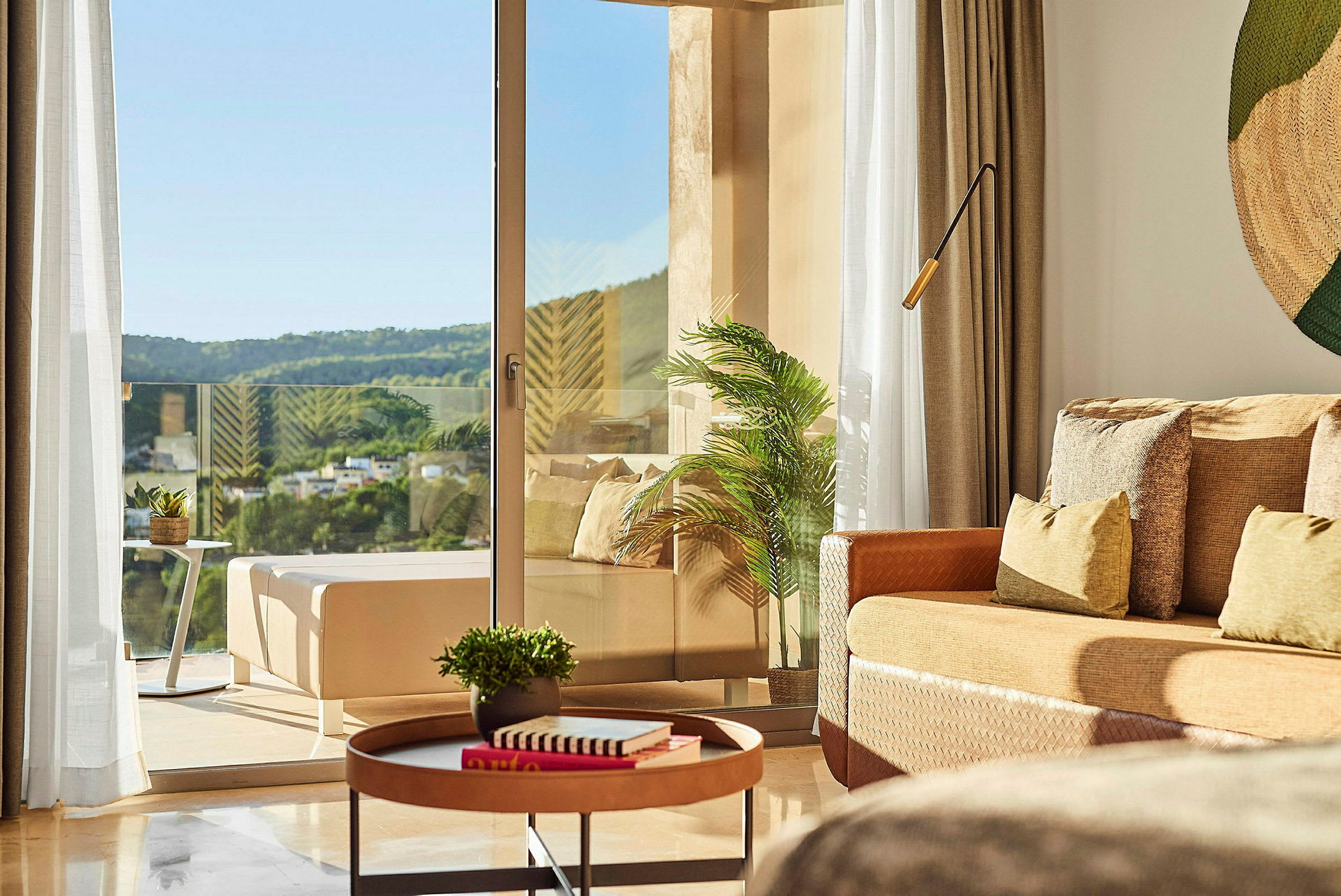 Ett ljust och modernt hotellrum med bord, växter och en utsikt mot naturen från balkongen. (AI-genererad text)