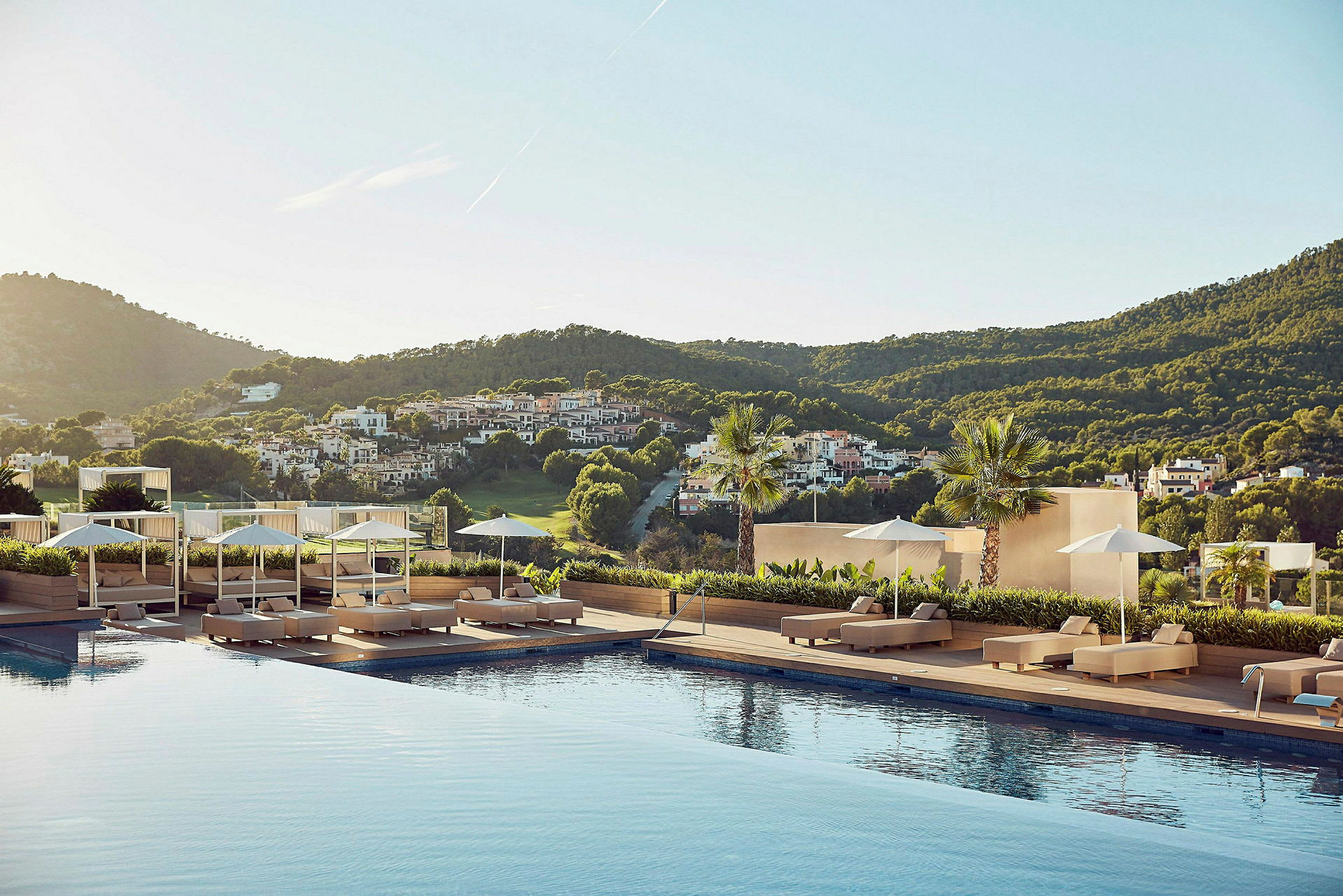 En utsikt från ett hotellområde med en pool omgiven av solstolar, parasoller och en grönskande landsbygd i bakgrunden. (AI-genererad text)