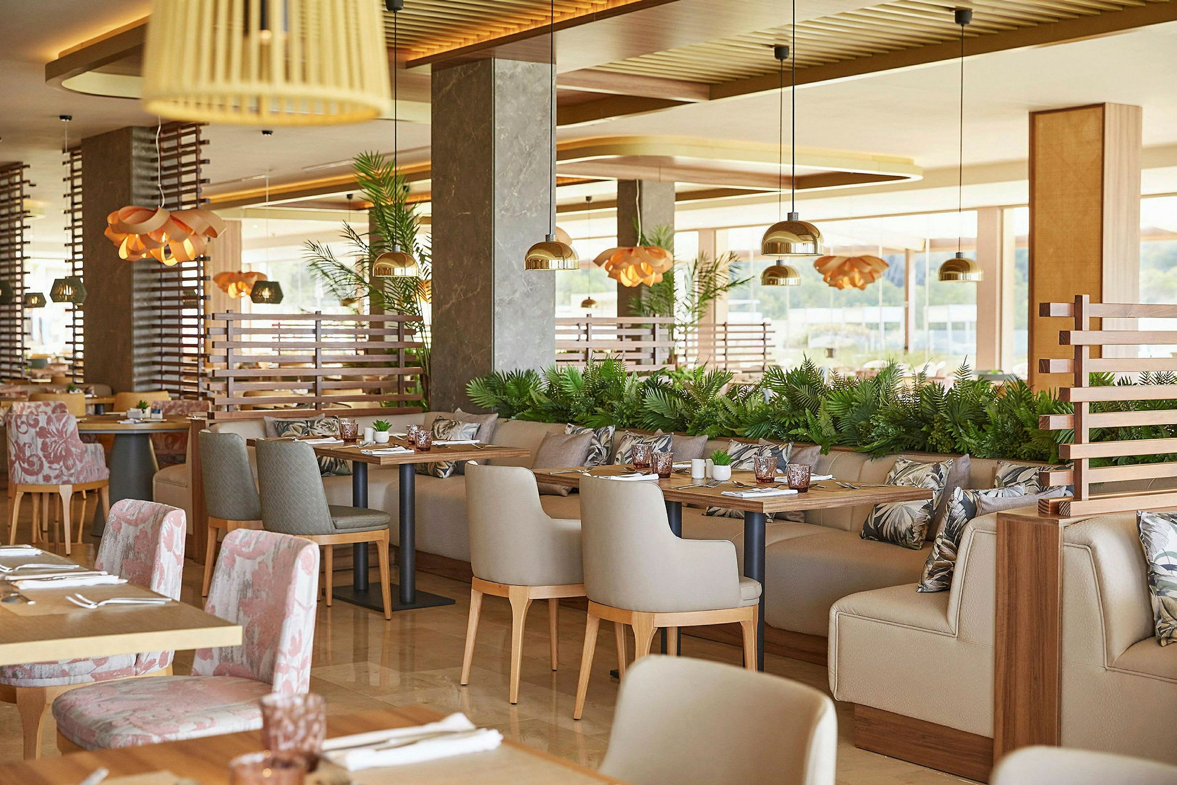 Ett modernt och elegant inrett restaurangområde med bord och stolar, dekorerat med växter och belysningsdetaljer. (AI-genererad text)