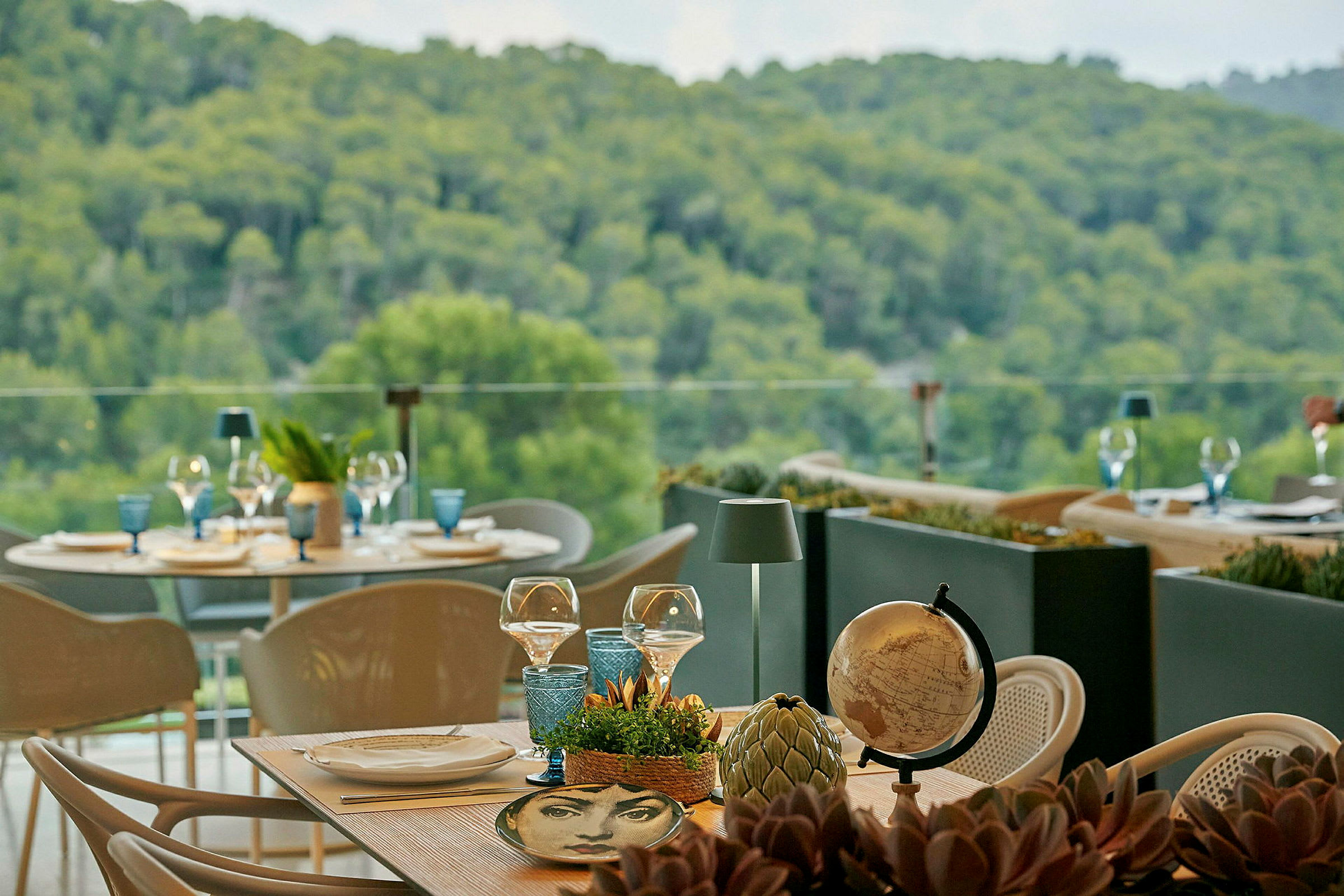 Utsikt över grönskande berg från en utomhusrestaurang med dukade bord. (AI-genererad text)