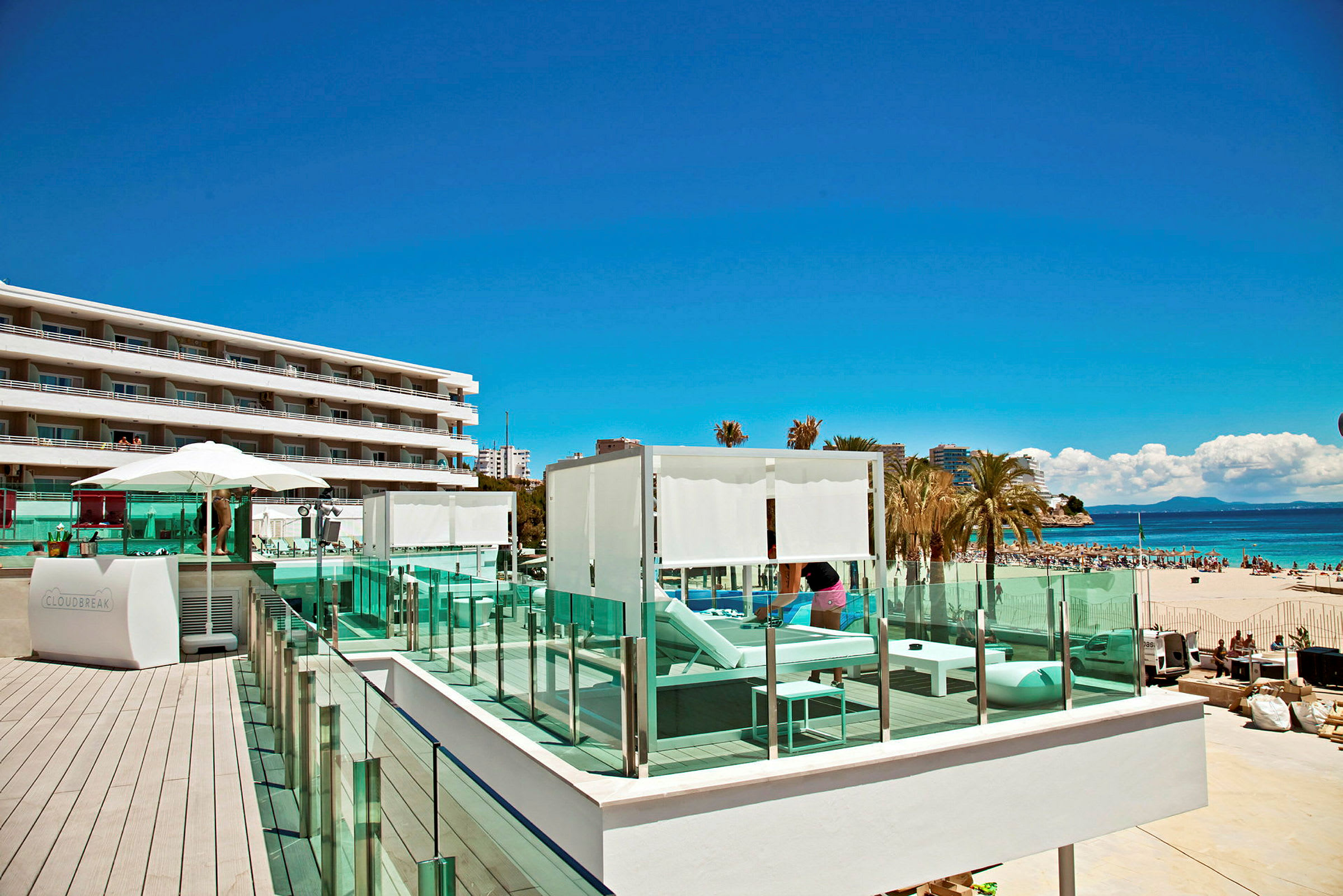 Ett hotellområde nära en strand, med solstolar och parasoller på en terrass. (AI-genererad text)