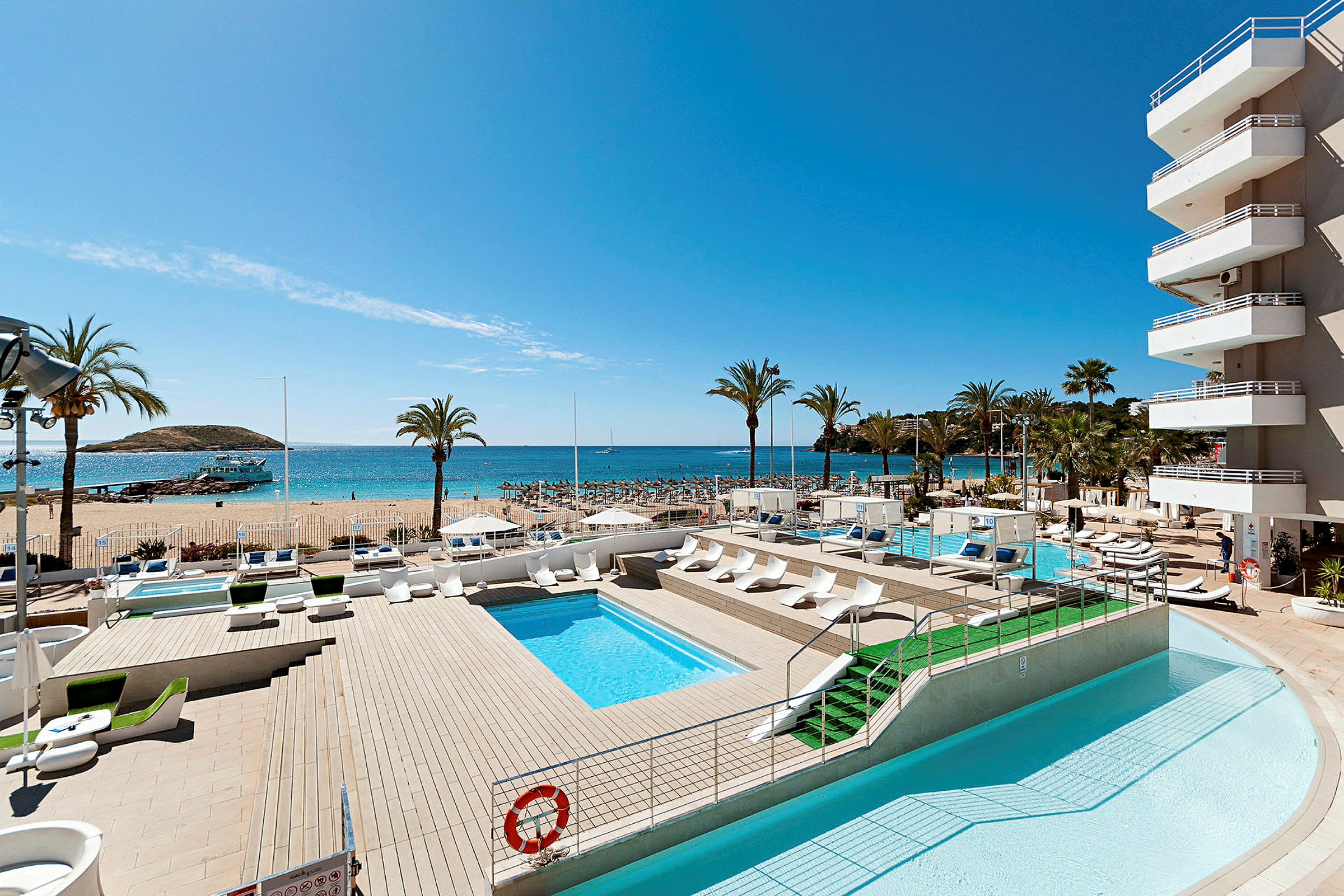 Bild av en hotellpool som vetter mot stranden och havet, omgiven av solstolar och palmer. (AI-genererad text)