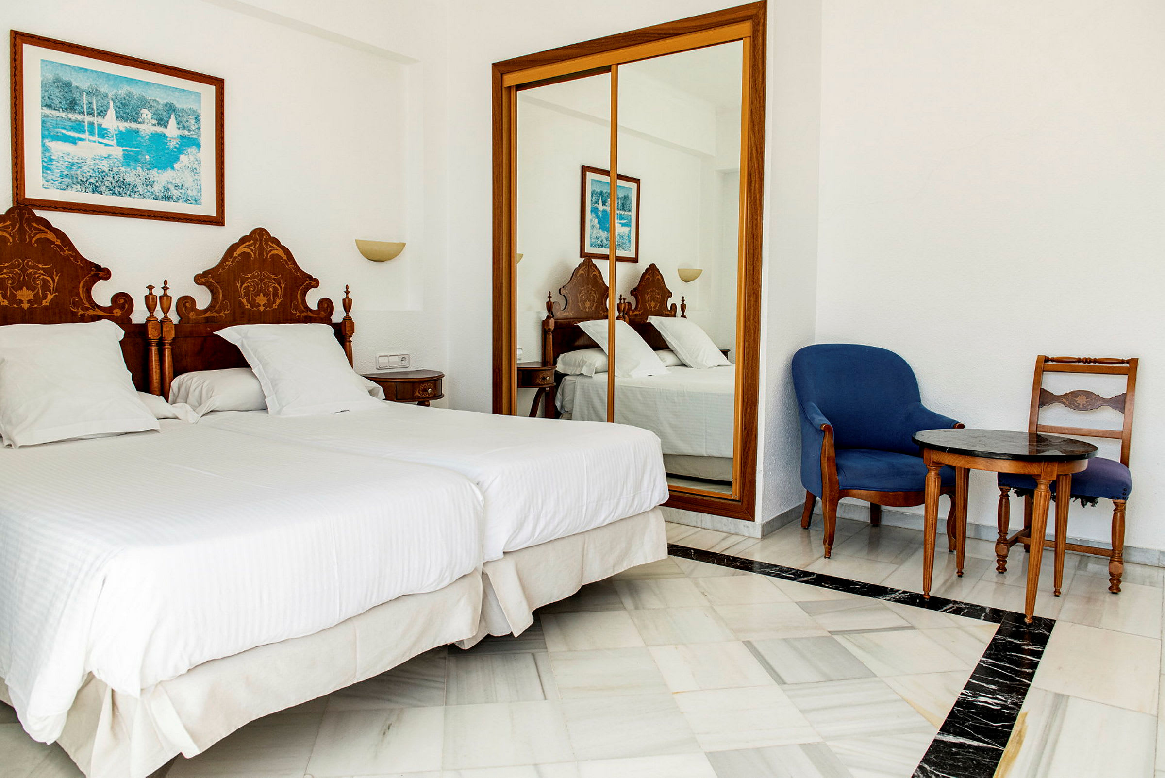 En hotellrum med två enkelsängar, en spegelgarderob och sittmöbler. (AI-genererad text)