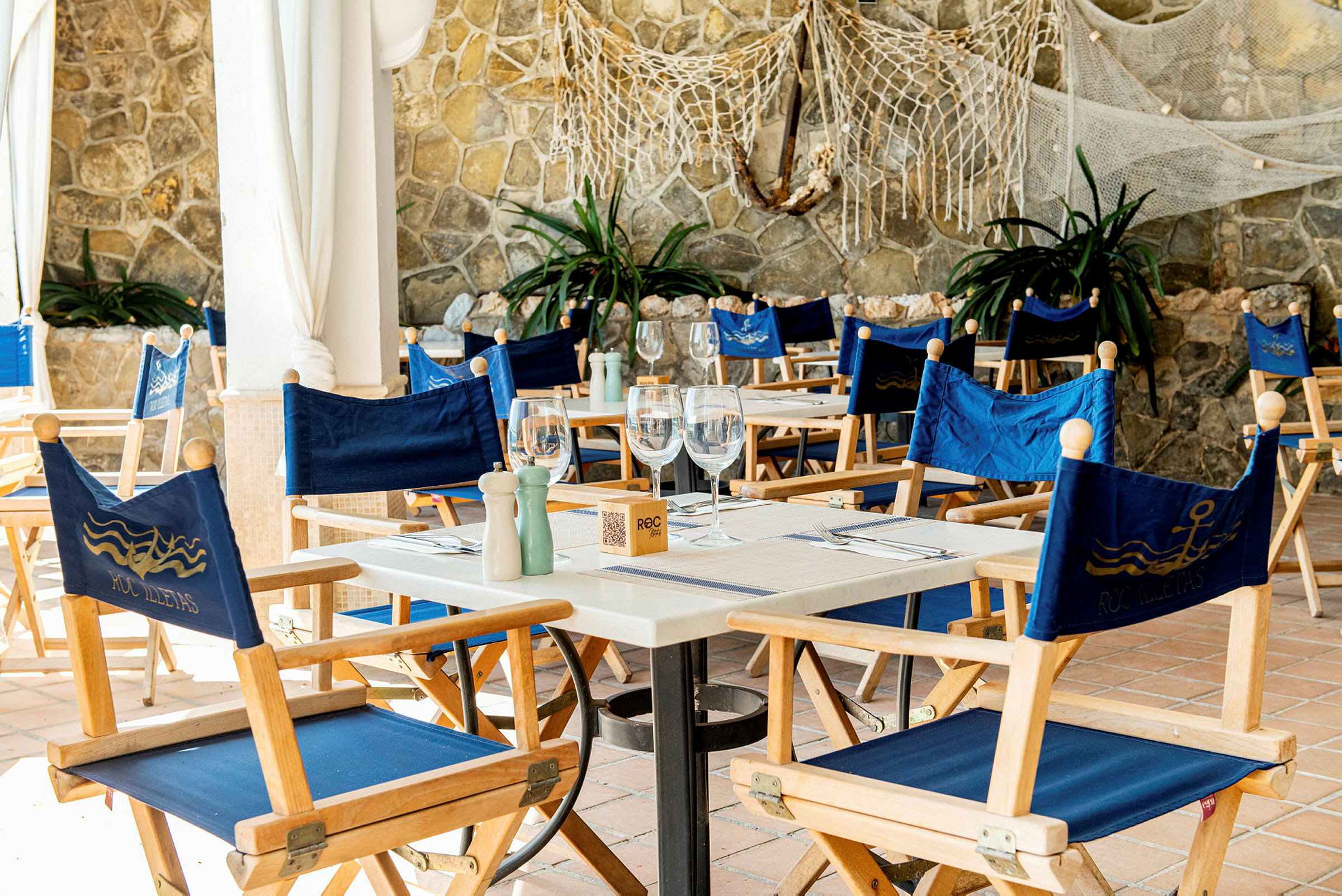 Ett bord med blå stolar på en restaurang med stenmur i bakgrunden. (AI-genererad text)