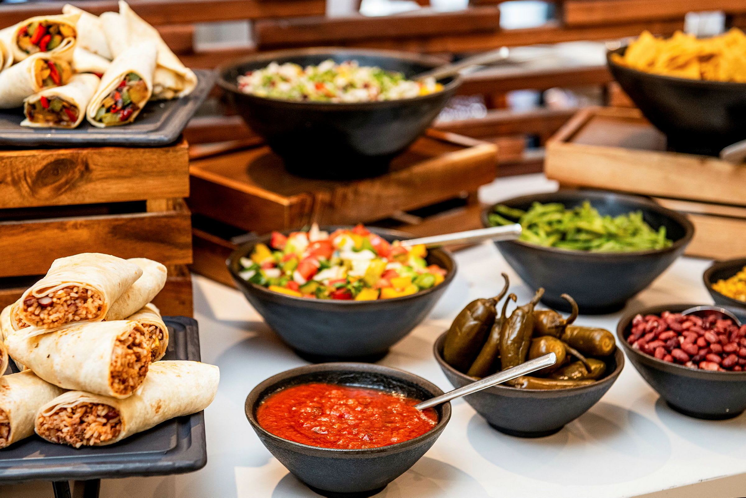 Bild av en buffé med burritos, sallad, jalapeños, sås och andra tillbehör. (AI-genererad text)