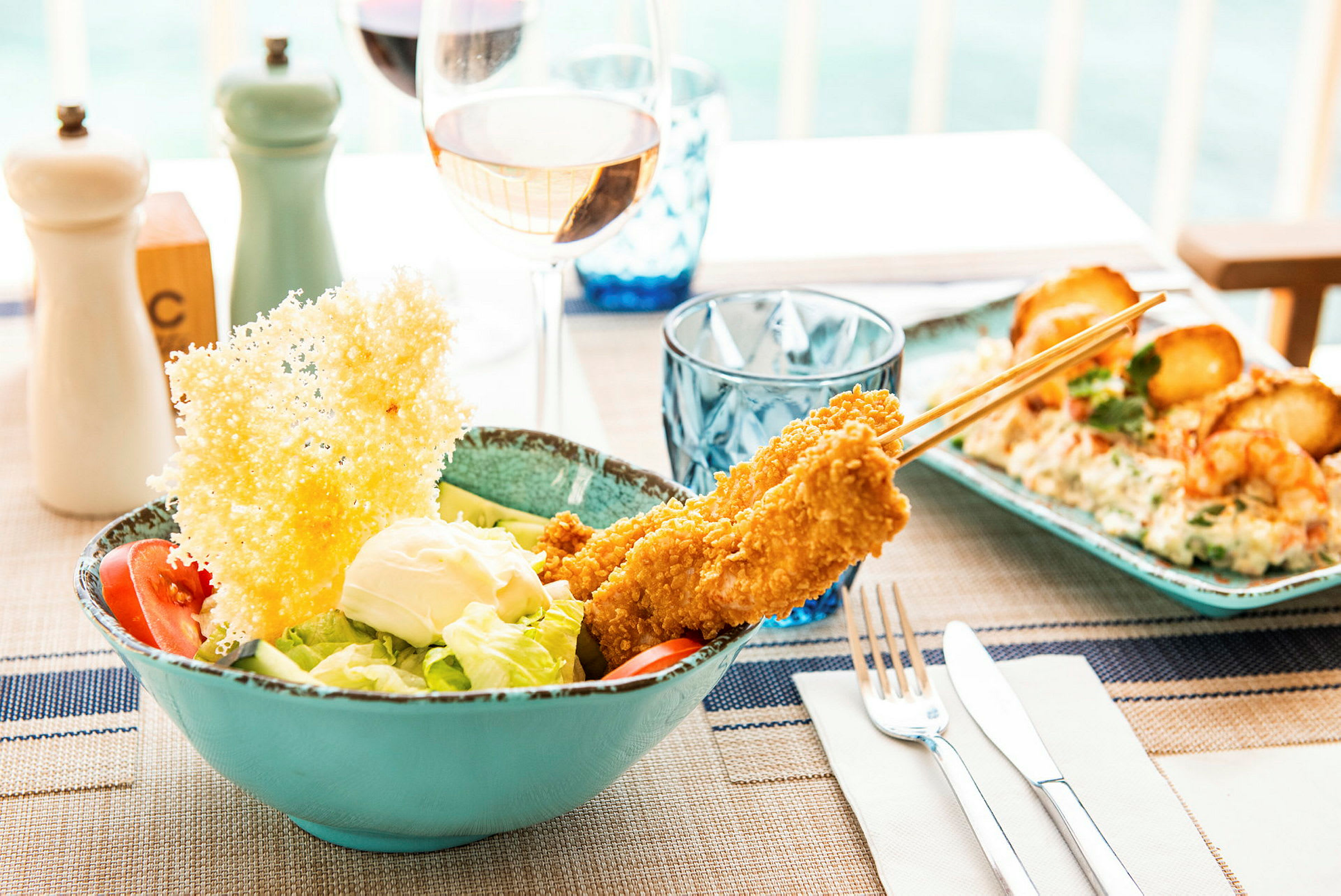 En sallad med tomat, sallad och dressing toppat med crispy kycklingspett och ett stort parmesanflarn på ett dukat bord. (AI-genererad text)