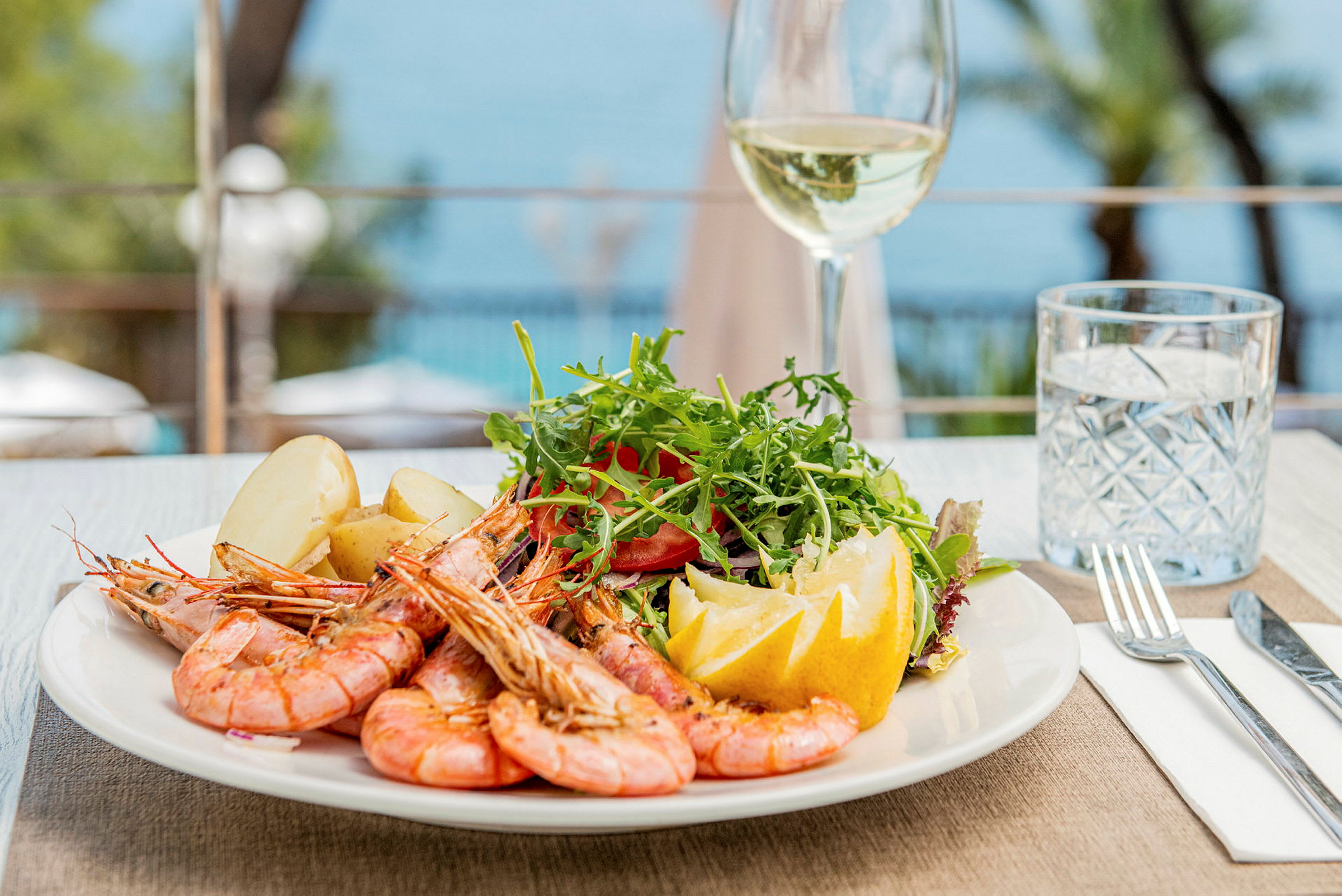 En tallrik med räkor, potatis, sallad och citron vid ett dukat bord. (AI-genererad text)