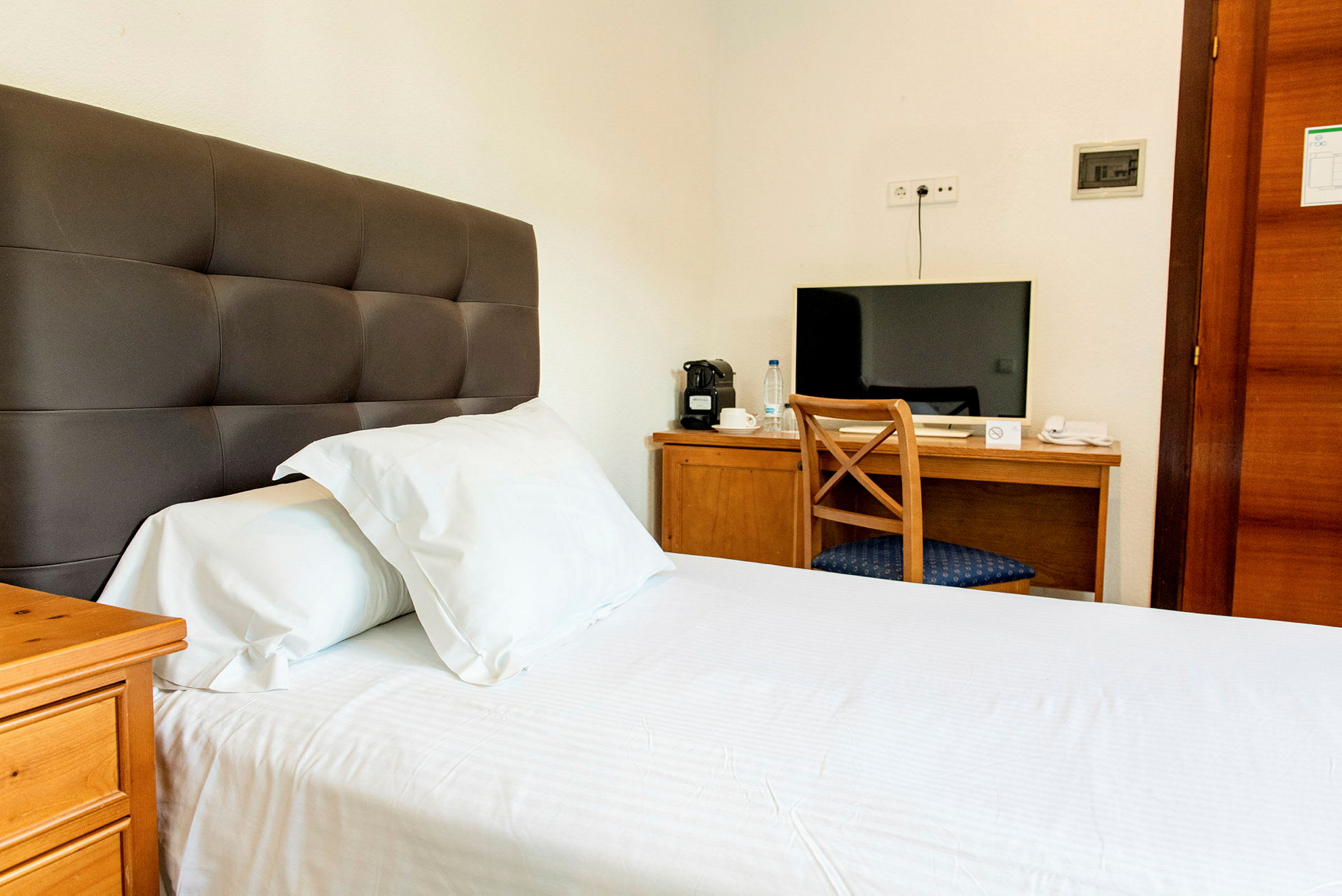Hotellrum med en säng och ett skrivbord med en stol och en TV. (AI-genererad text)