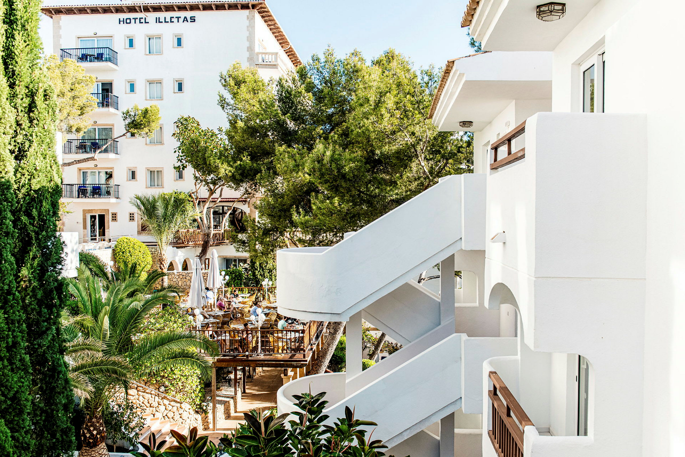 Vit byggnad med Hotel Illetas. Grönska och träd vid sidan. (AI-genererad text)