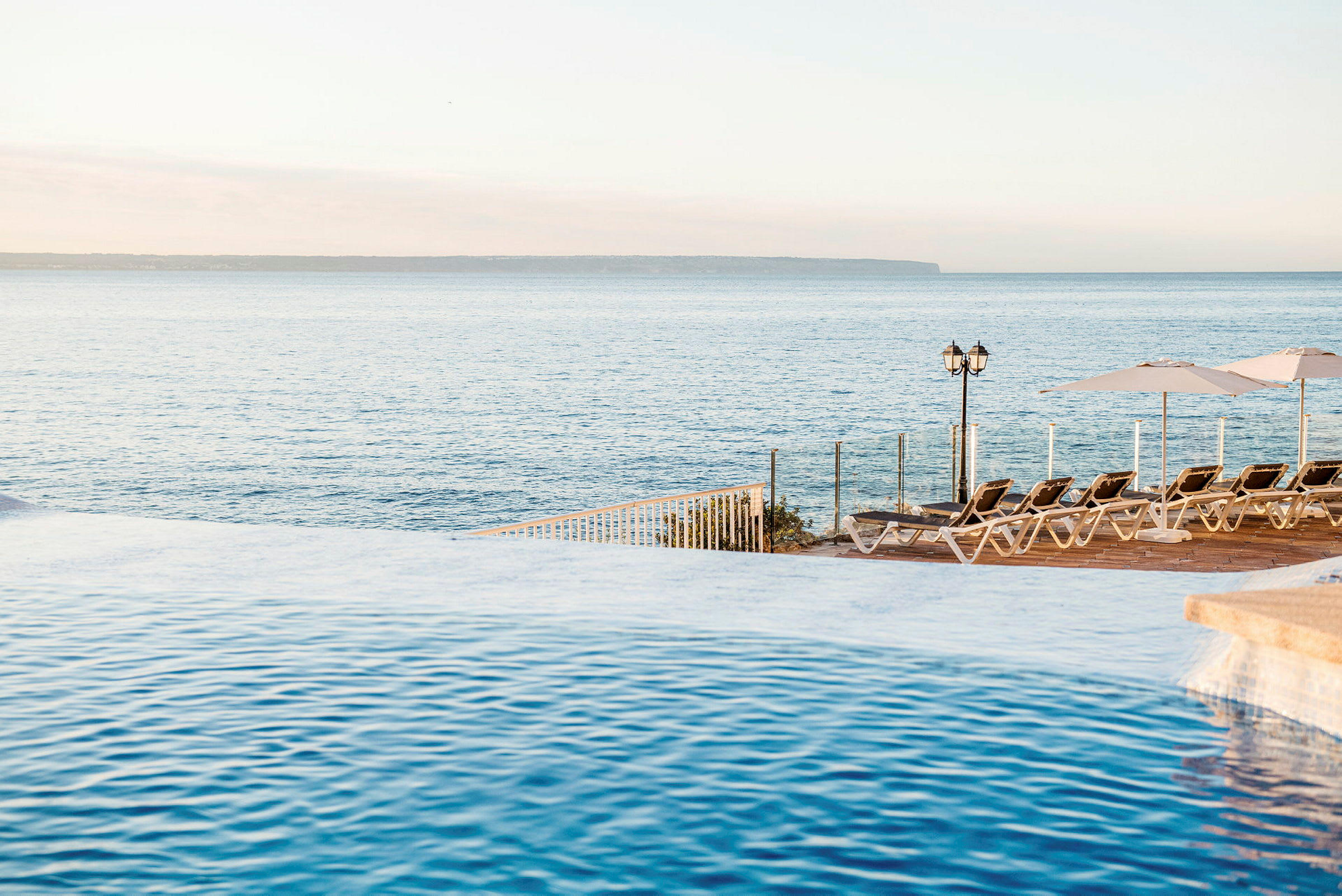 Pool med utsikt över havet och solstolar på terrass. (AI-genererad text)