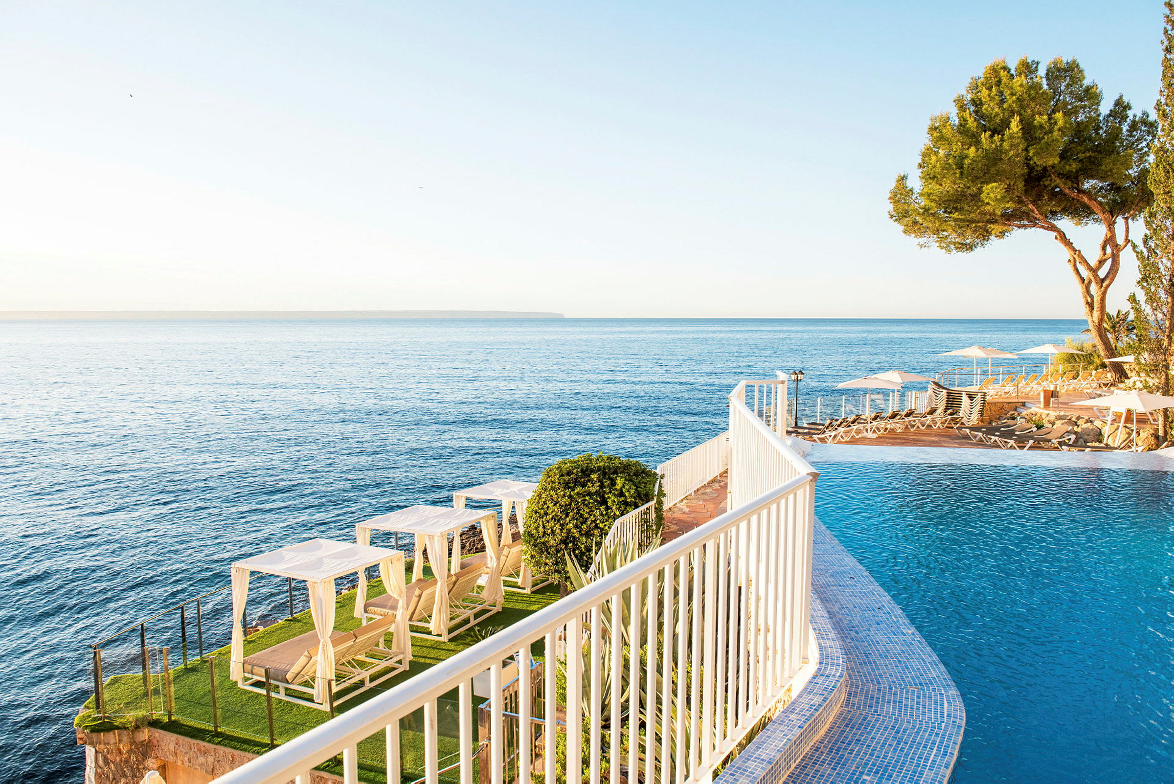 En infinitypool vid havet med solstolar och omslutande grönska. (AI-genererad text)