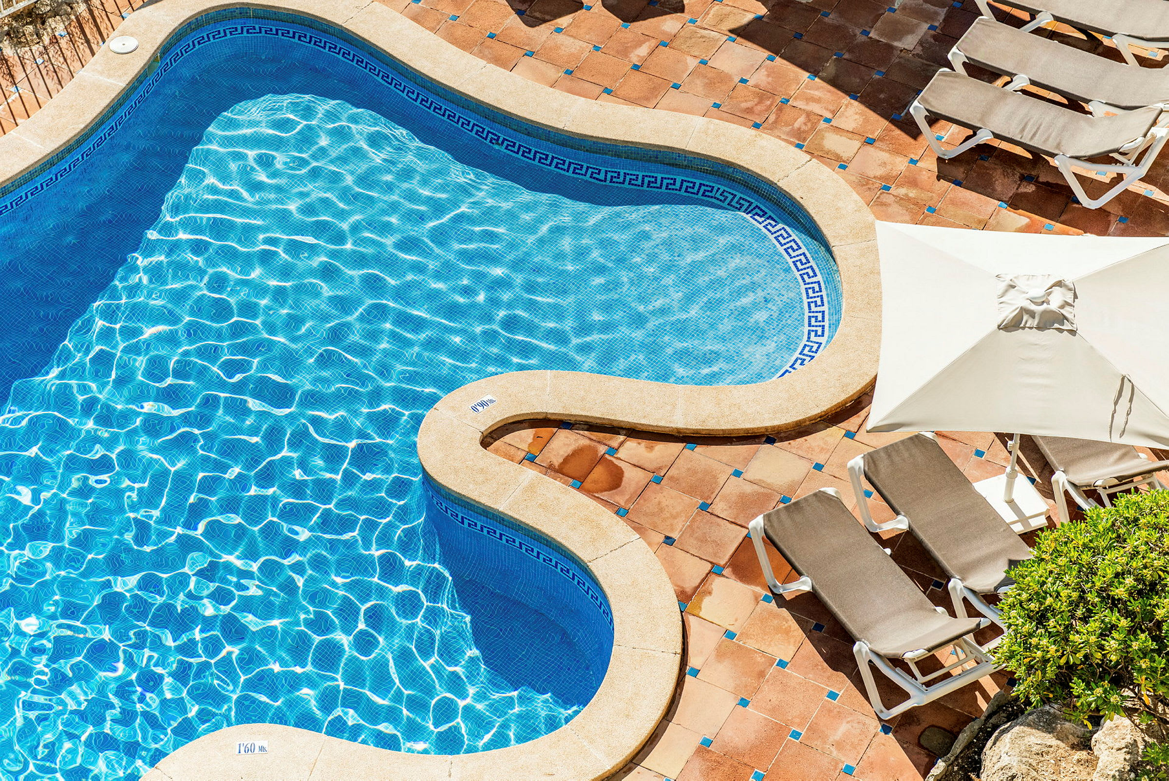 En formad swimmingpool med blått vatten och omgivande solstolar på stenbelagd yta. (AI-genererad text)