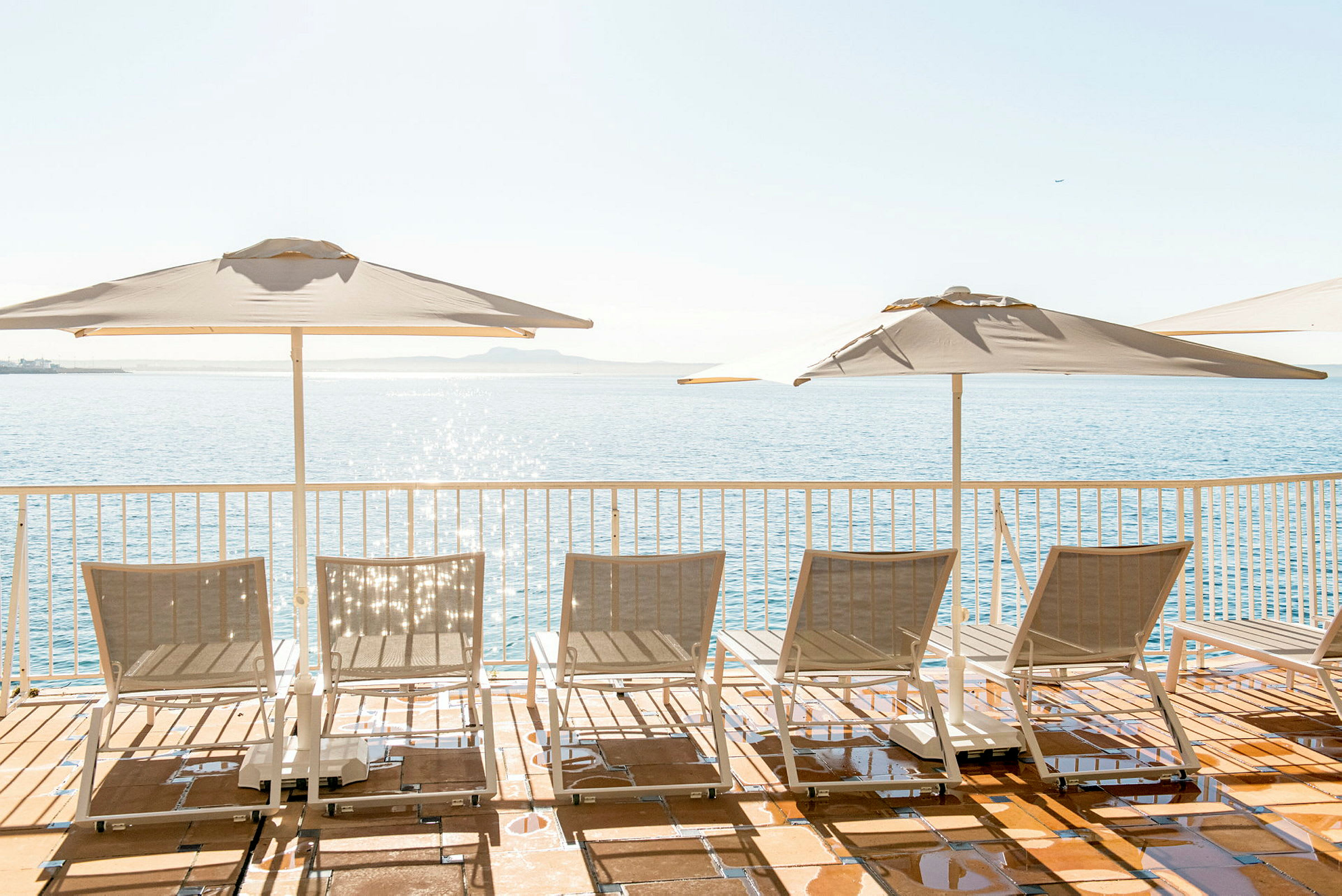 Solstolar och parasoller vid en terrass med utsikt över havet. (AI-genererad text)