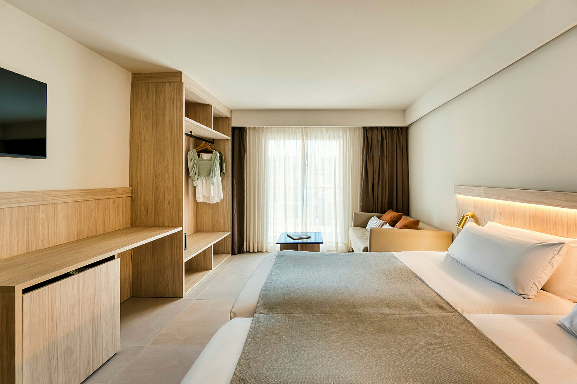 Ett hotellrum med en dubbelsäng, skrivbord och garderob. Fönstret är täckt med ljusa gardiner. (AI-genererad text)