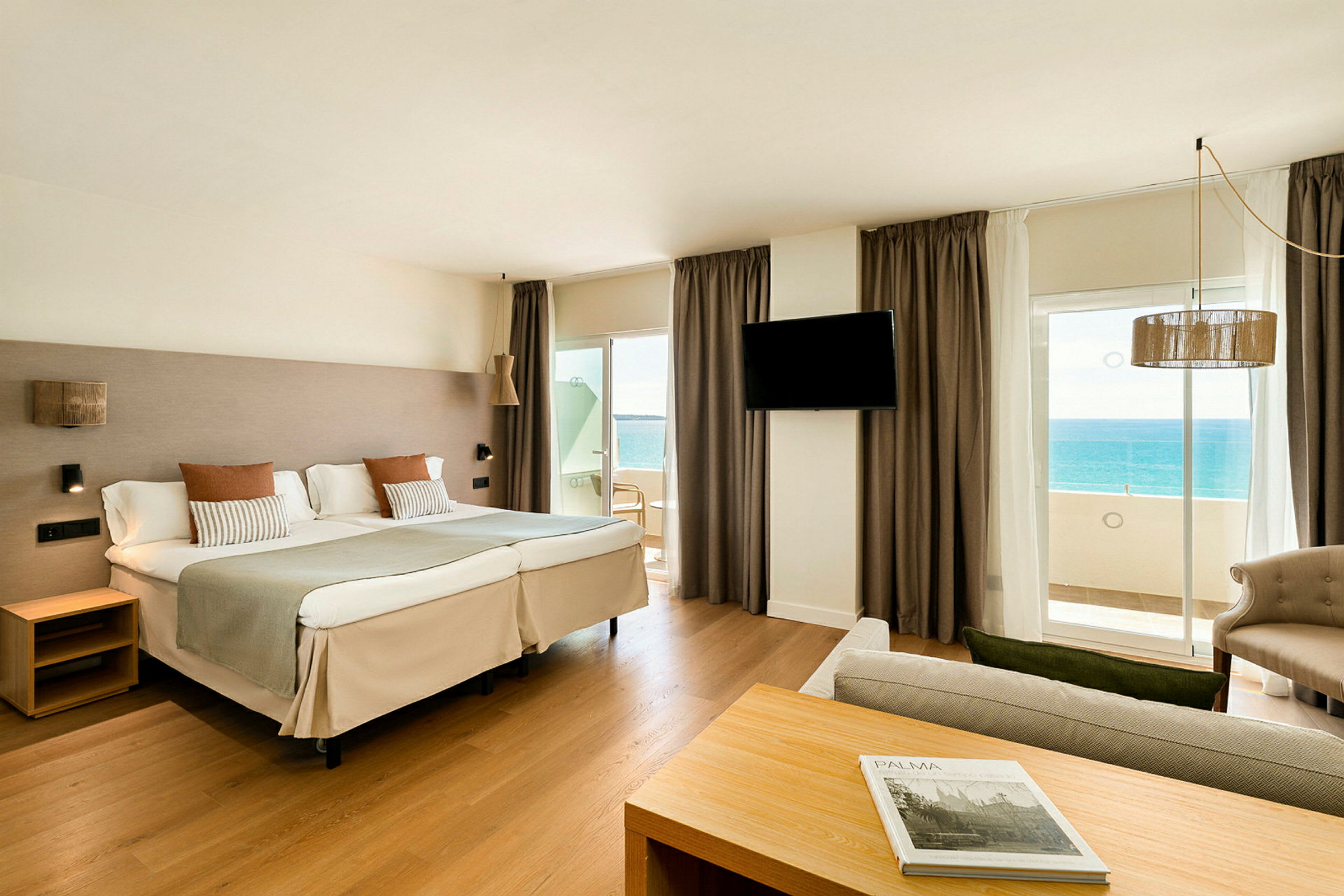 Ett hotellrum med två sängar, en TV på väggen och stora fönster som vetter mot havet. (AI-genererad text)