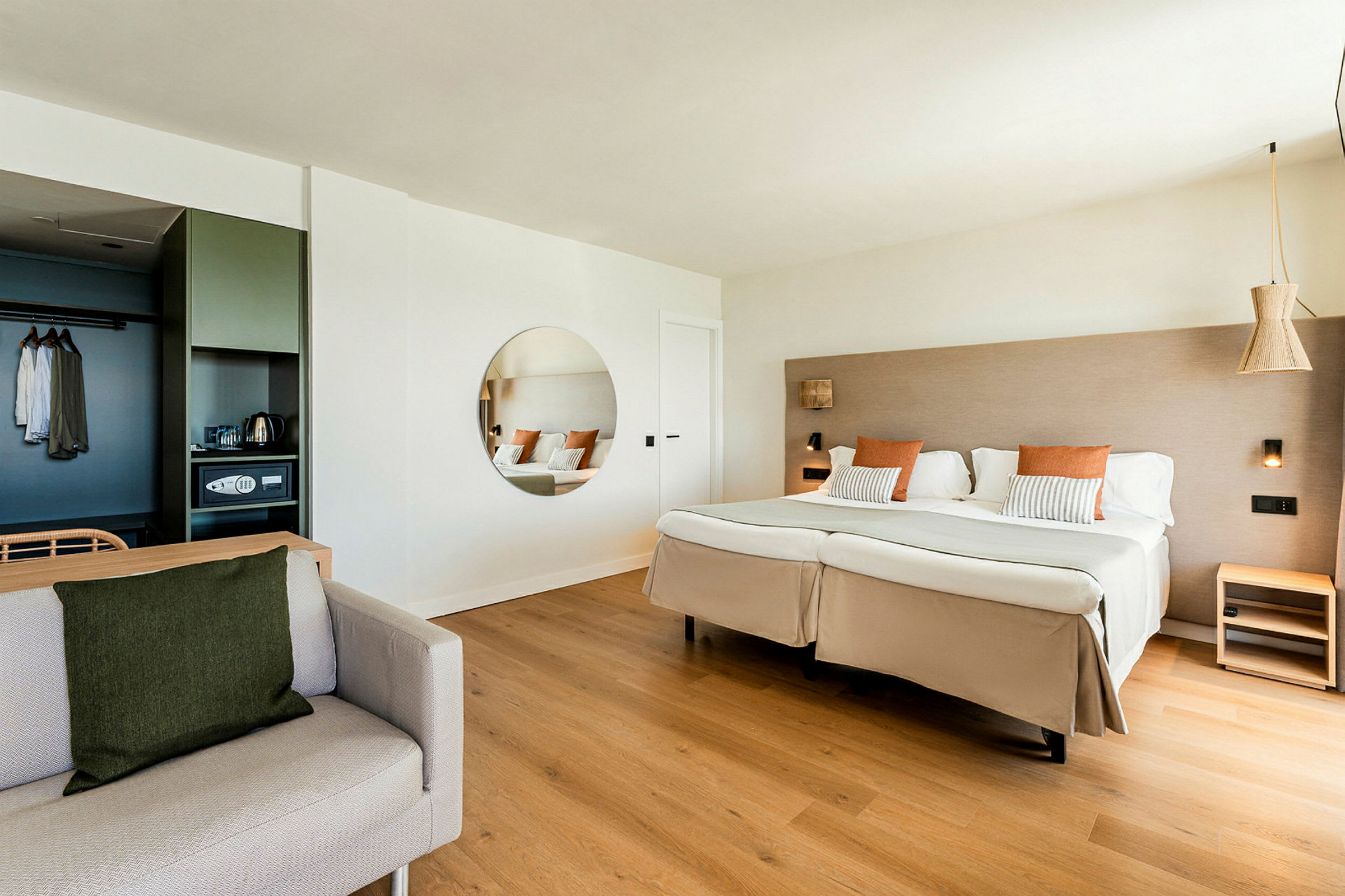 Ett hotellrum med en stor dubbelsäng, en rund spegel på väggen och en soffa i förgrunden. (AI-genererad text)