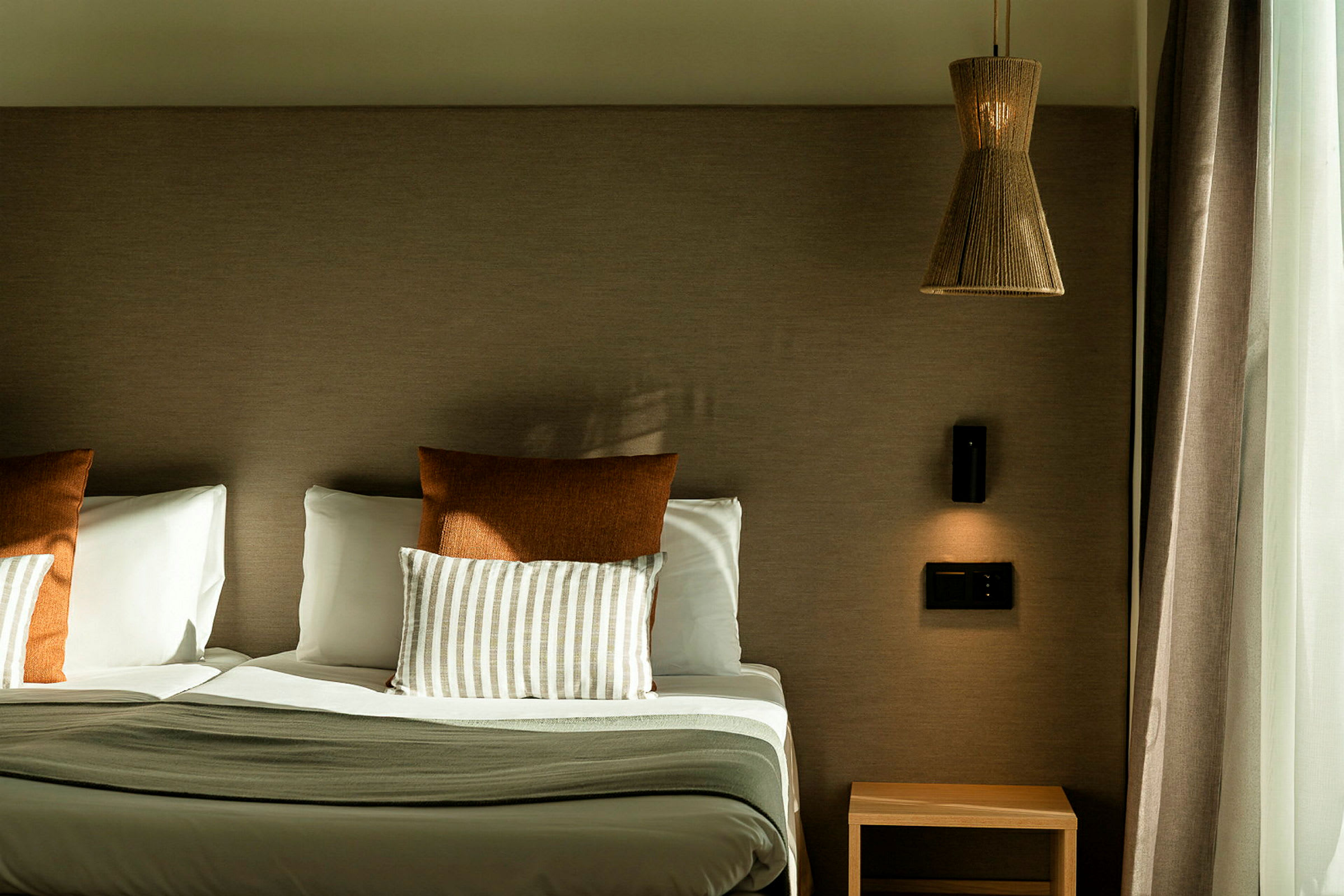 Hotellsäng med två kuddar, ett nattduksbord och en lampa på väggen. (AI-genererad text)