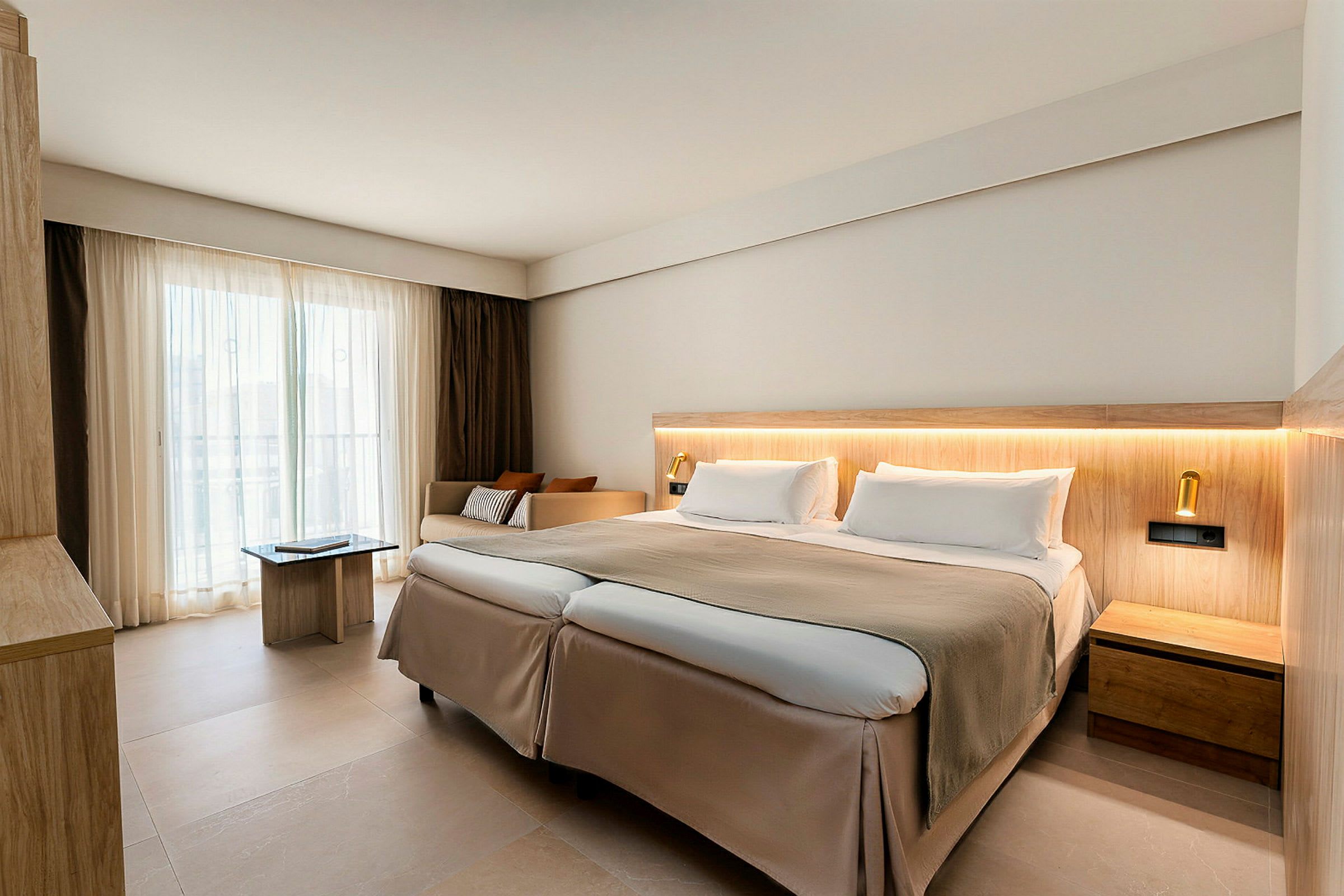 En modern hotellrum med en dubbelsäng, ljusa färger och stora fönster med gardiner. (AI-genererad text)