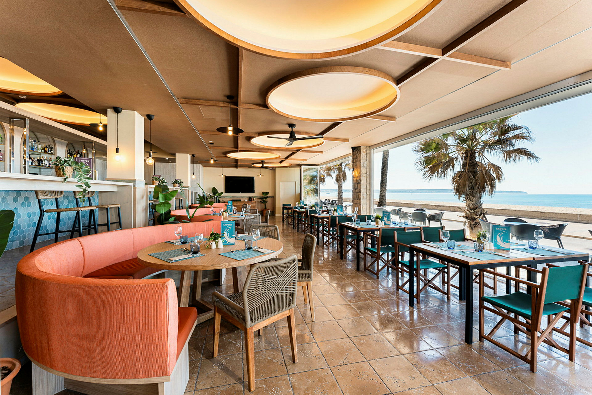 Restaurang med moderna möbler och stora fönster som vetter mot en strand. (AI-genererad text)