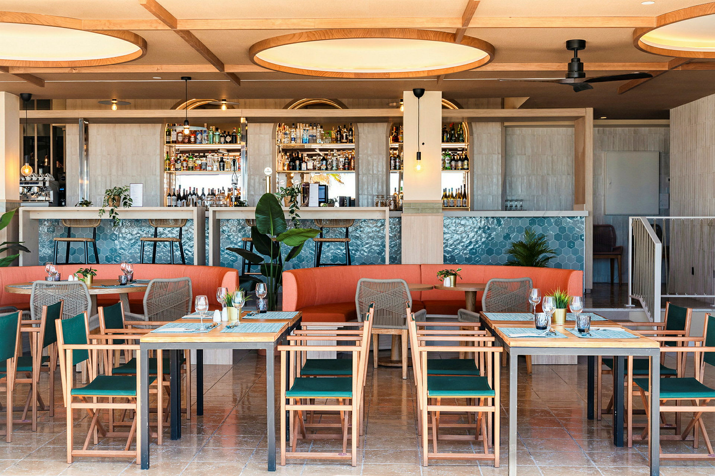 Bild på en modern restaurang med bord, stolar och en orange soffa samt en bartender som är dekorerad med blått kakel. (AI-genererad text)
