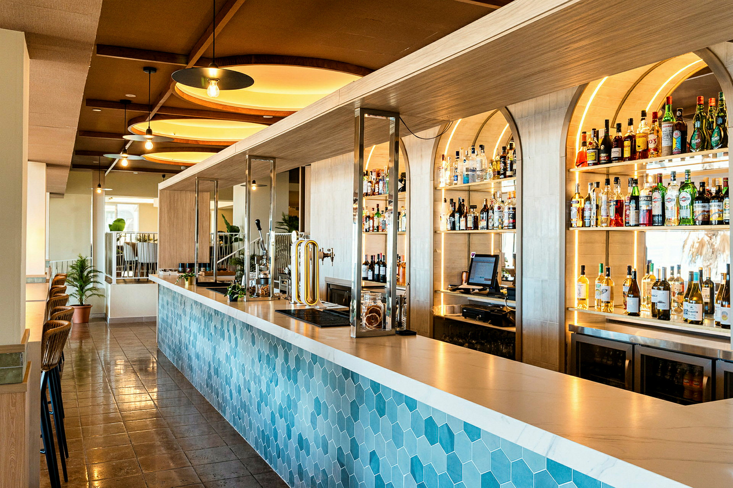 En modern bar med en blå hexagonmönstrad bardisk och hyllor fyllda med flaskor och drycker i bakgrunden. (AI-genererad text)