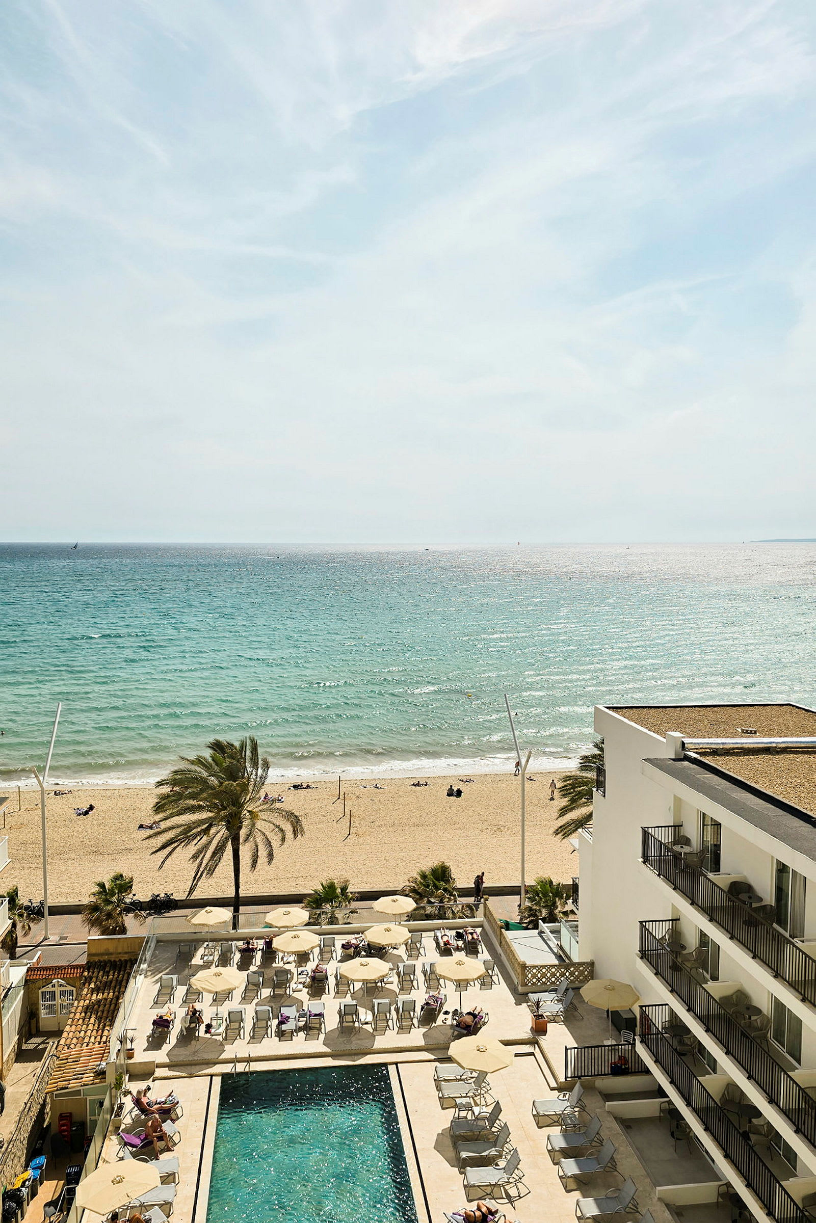 En sandstrand vid havet med solstolar och parasoller vid en hotellpool. (AI-genererad text)