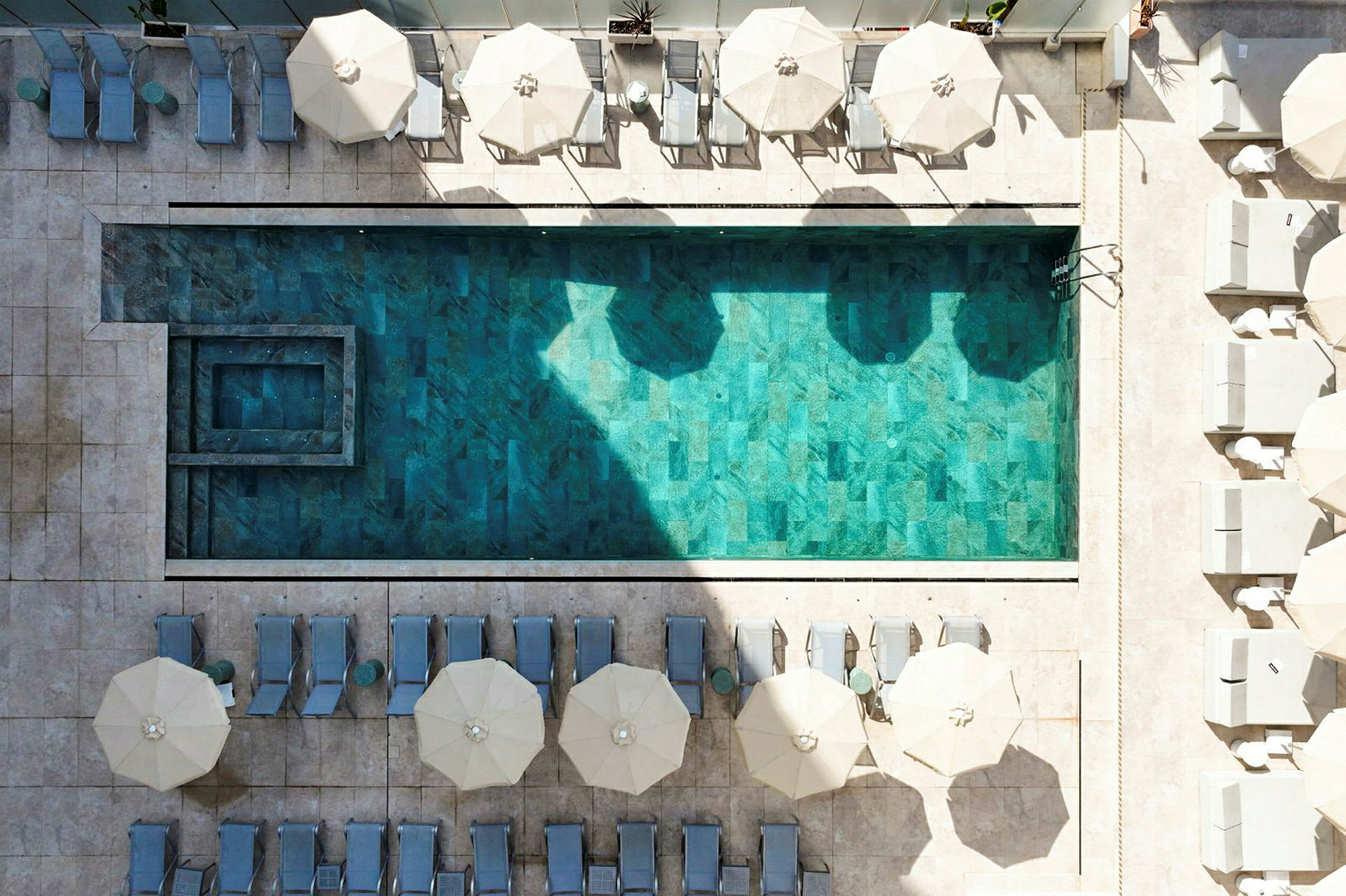 Bild på en rektangulär pool med omgivande solstolar och parasoller, sedd från ovan. (AI-genererad text)