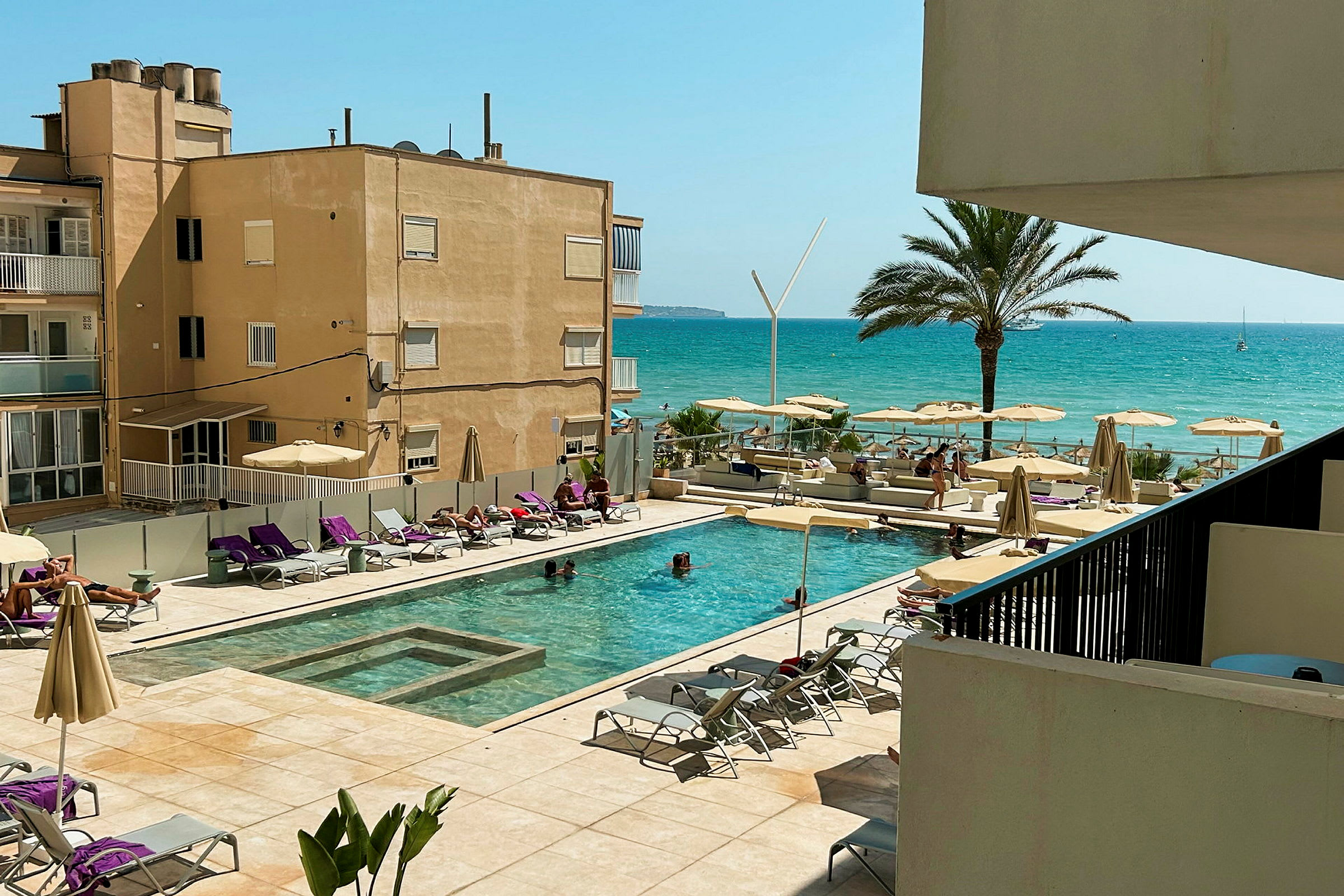 Utsikt över en hotellpool med solstolar och parasoller, med en strand och havet i bakgrunden. (AI-genererad text)