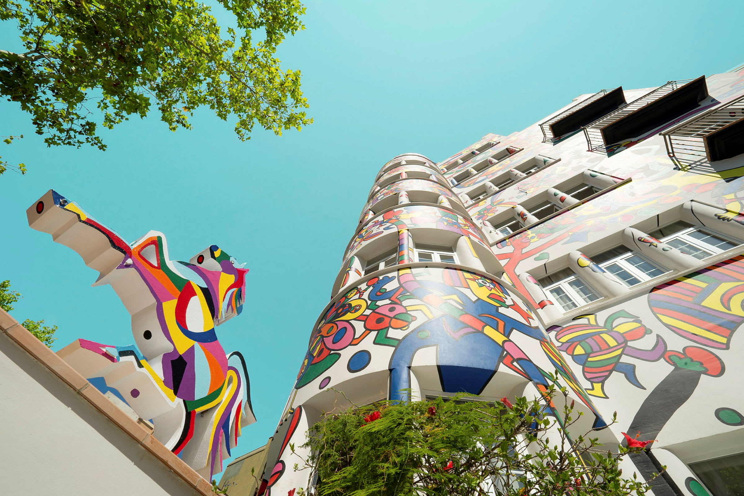 Bild av en färgglad byggnad med abstrakt konst och en staty av en häst i vibrant färger under en klar himmel. (AI-genererad text)