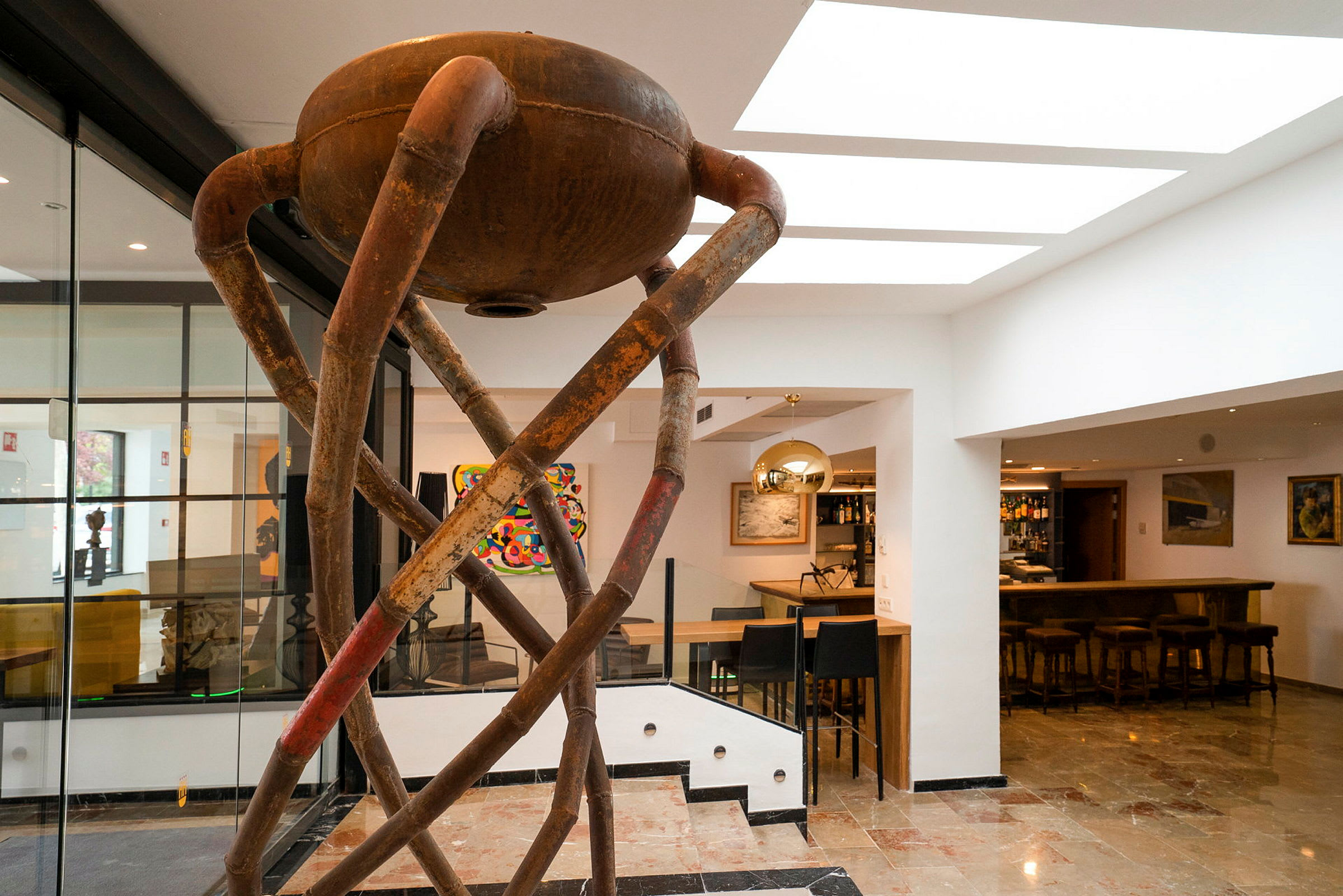 Interiör med en modern skulptur med rustrött metallrör. I bakgrunden syns en bar och olika konstverk. (AI-genererad text)