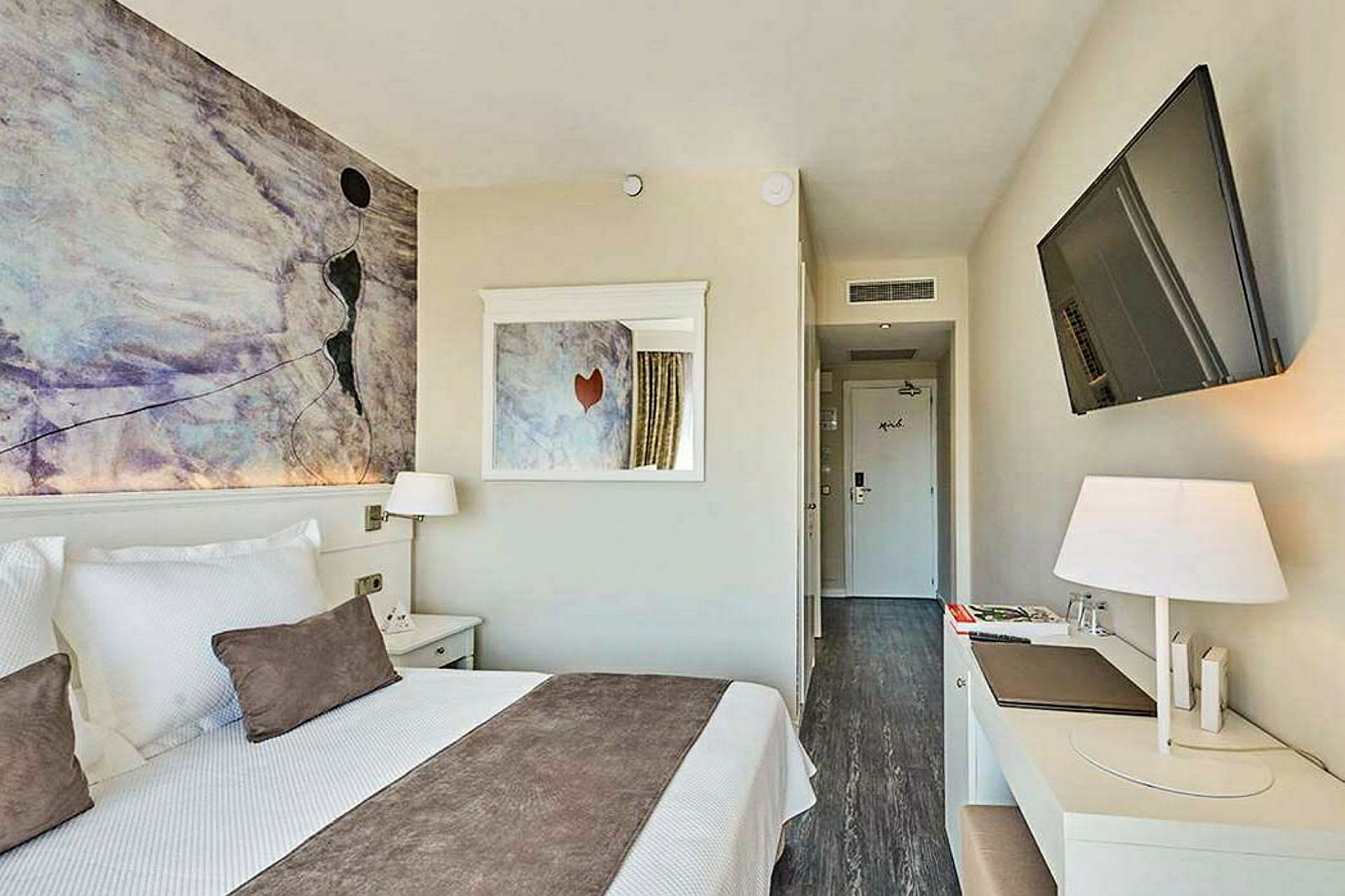 Ett modernt hotellrum med en dubbelsäng, väggkonst, skrivbord och platt-TV. (AI-genererad text)