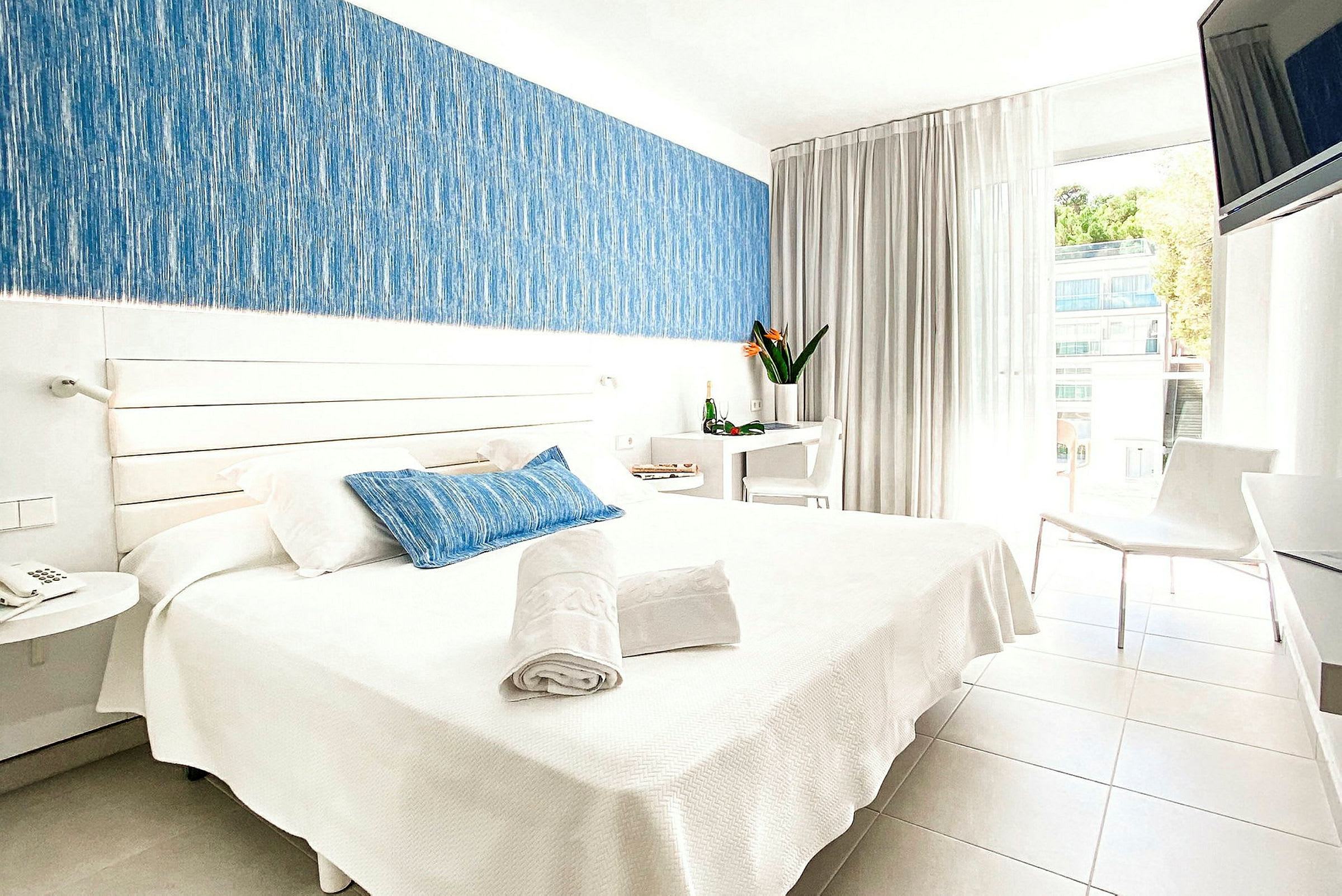 Bild på ett ljust hotellrum med en dubbelsäng, vita möbler och detaljer i blått. (AI-genererad text)