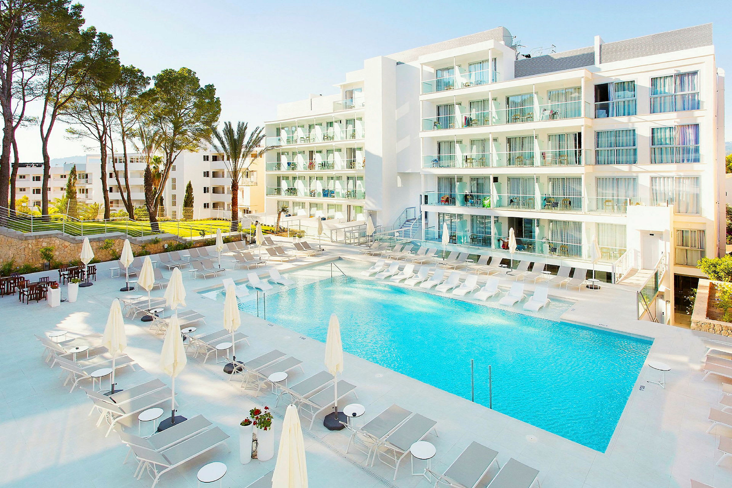 Ett modernt hotellkomplex med en pool omgiven av solstolar och parasoller. (AI-genererad text)