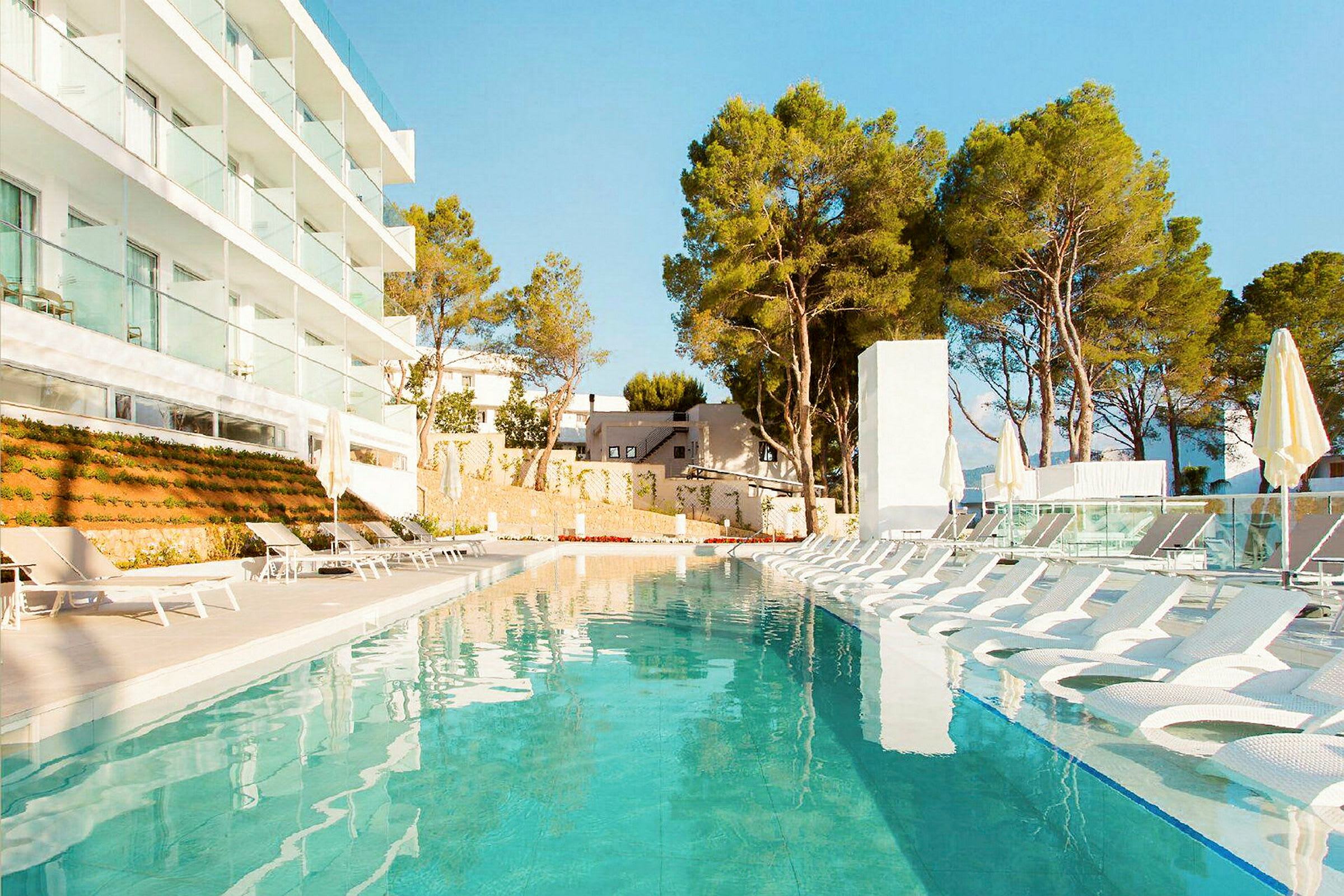 En utomhuspool vid ett modernt hotell med omgivande solstolar och grönska i bakgrunden. (AI-genererad text)