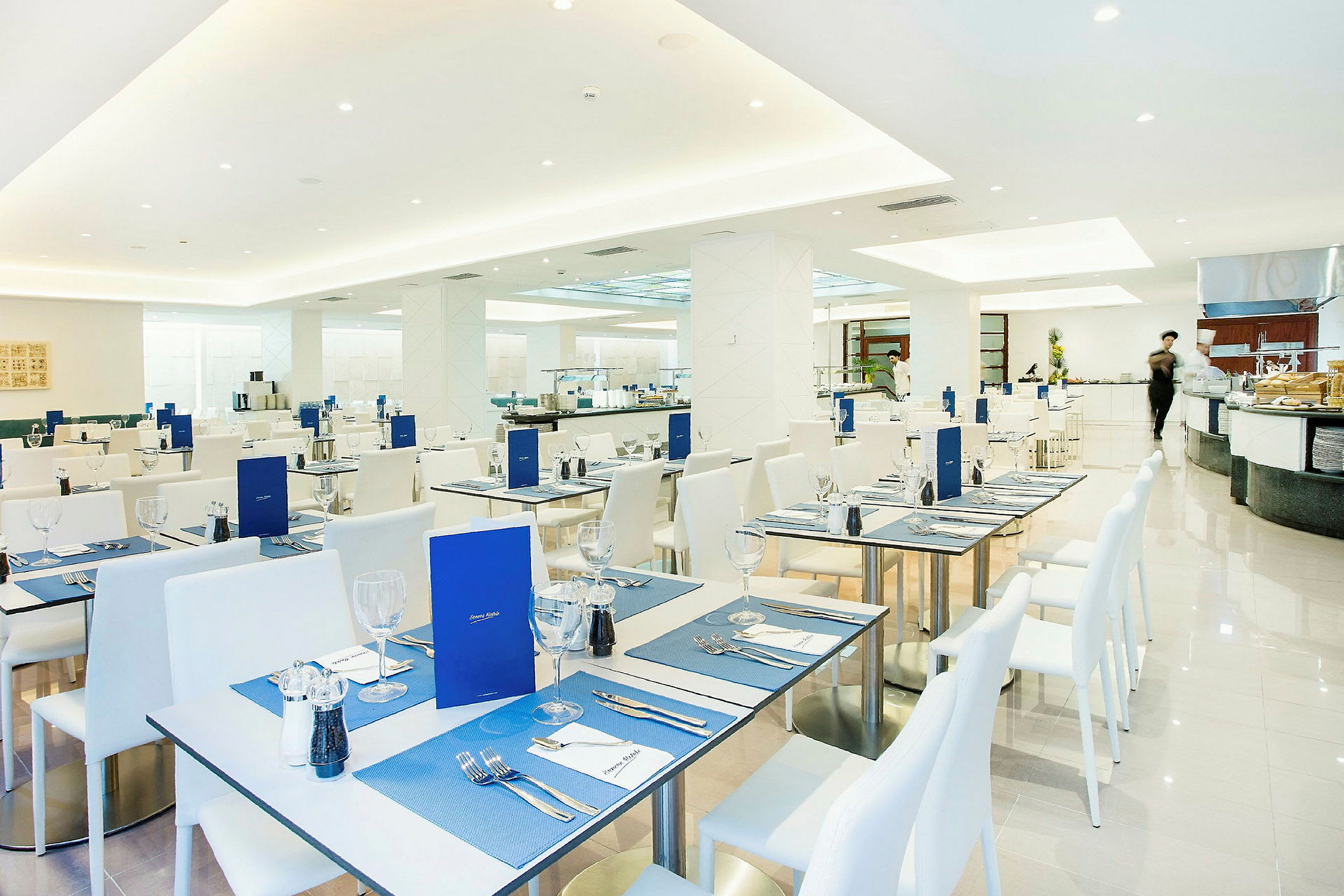 Restaurang med vita bord och stolar, dukade med blå bordstabletter och menyer. (AI-genererad text)