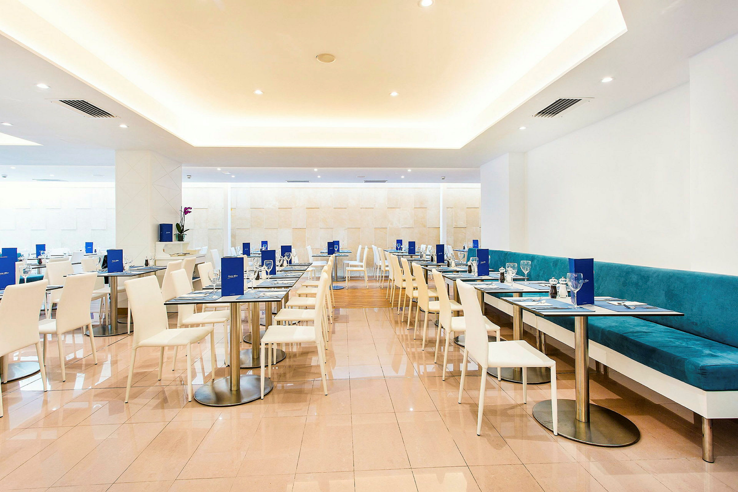 Interiör av en modern restaurang med vita stolar och bord samt turkosa soffor. (AI-genererad text)