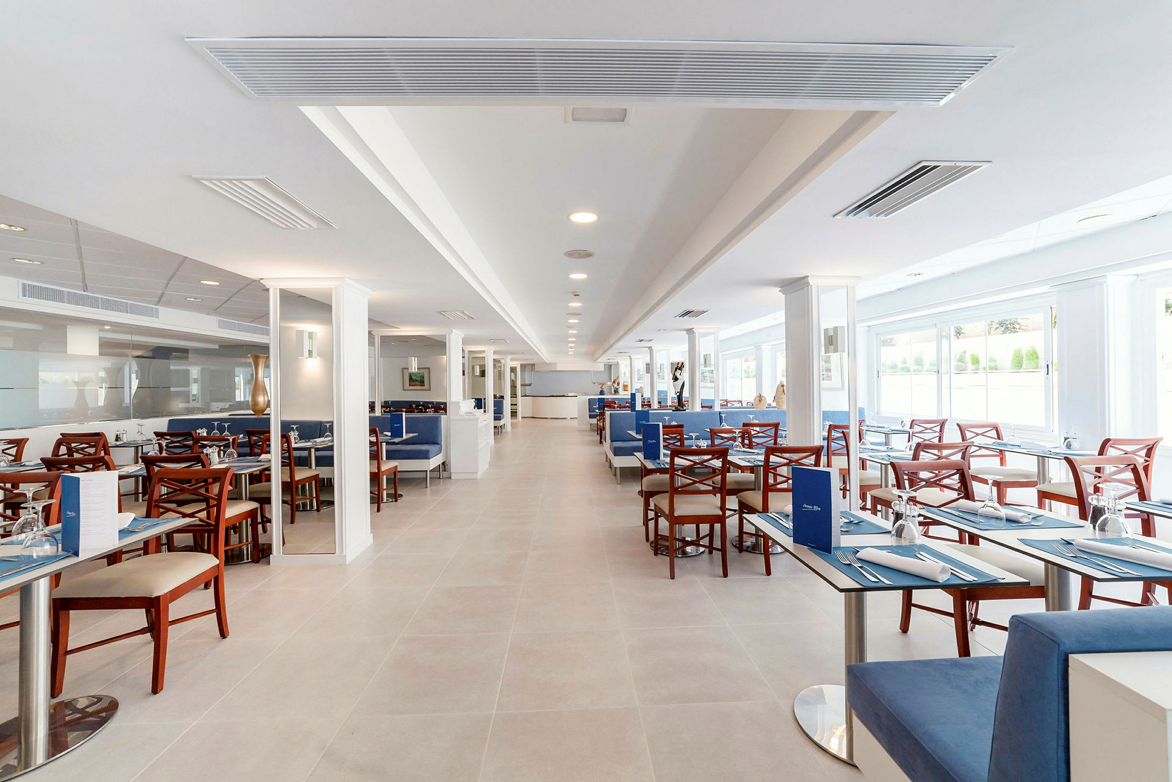 En restaurang med uppdukade bord och stolar, ljus och modern inredning med stora fönster. (AI-genererad text)