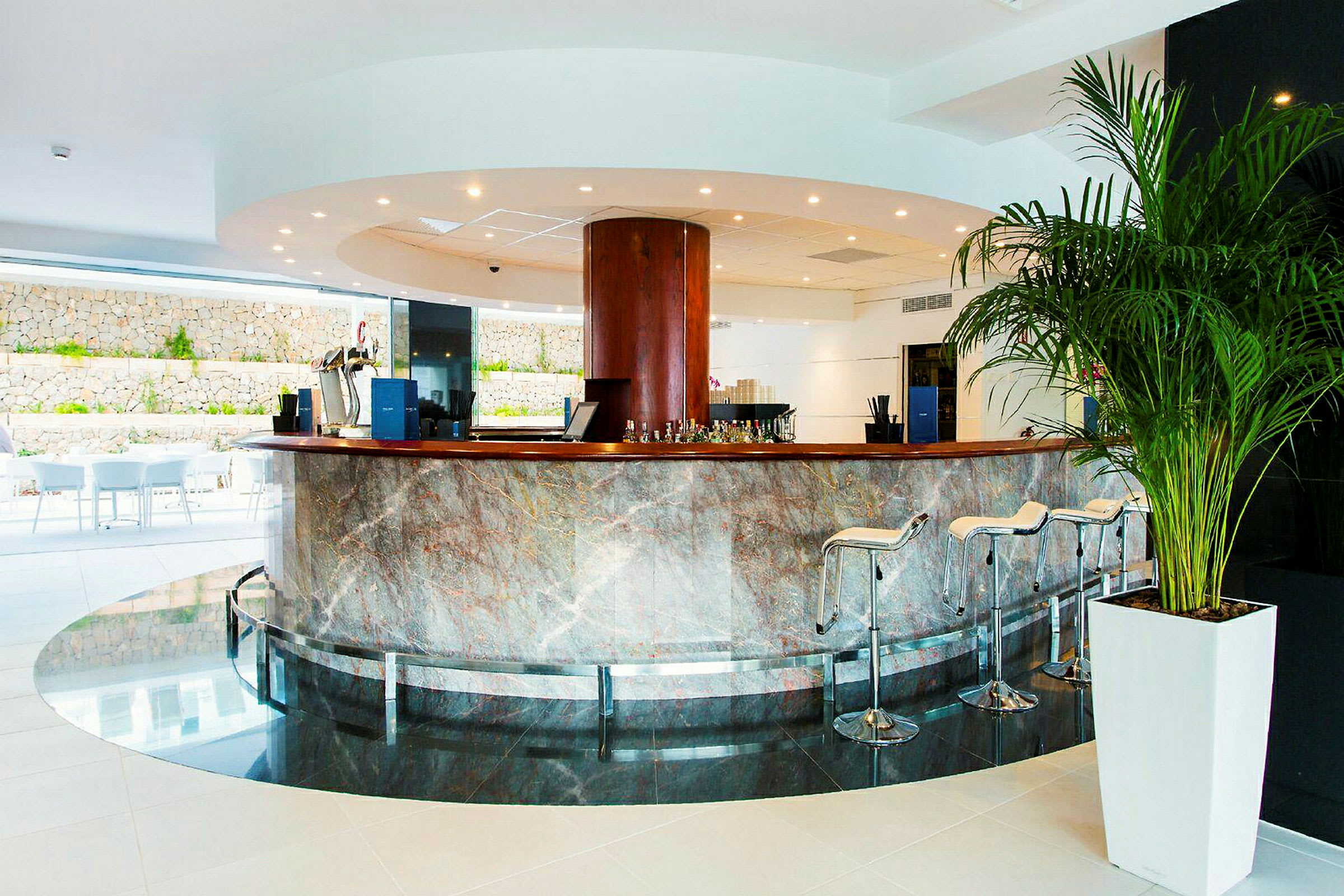 En modern hotellobby med en centralt placerad rund disk, omgiven av höga stolar och utsmyckad med polerad sten. (AI-genererad text)