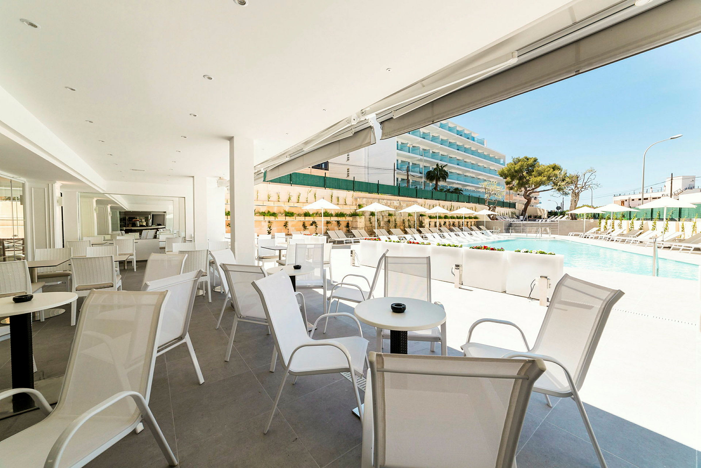En ljus uteservering med stolar och bord i vitt, med utsikt över en pool och solstolar. (AI-genererad text)