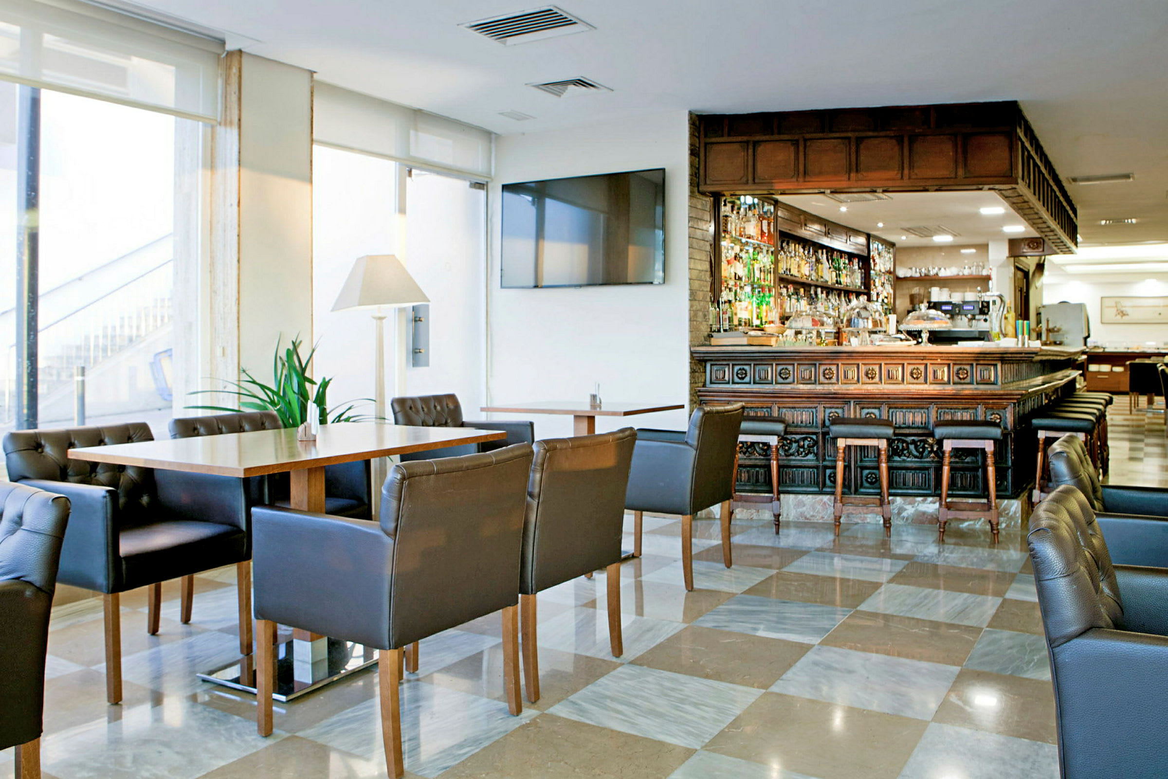 Ett hotellbarområde med bord, stolar och en välfylld bardisk i ett elegant och ljust rum. (AI-genererad text)