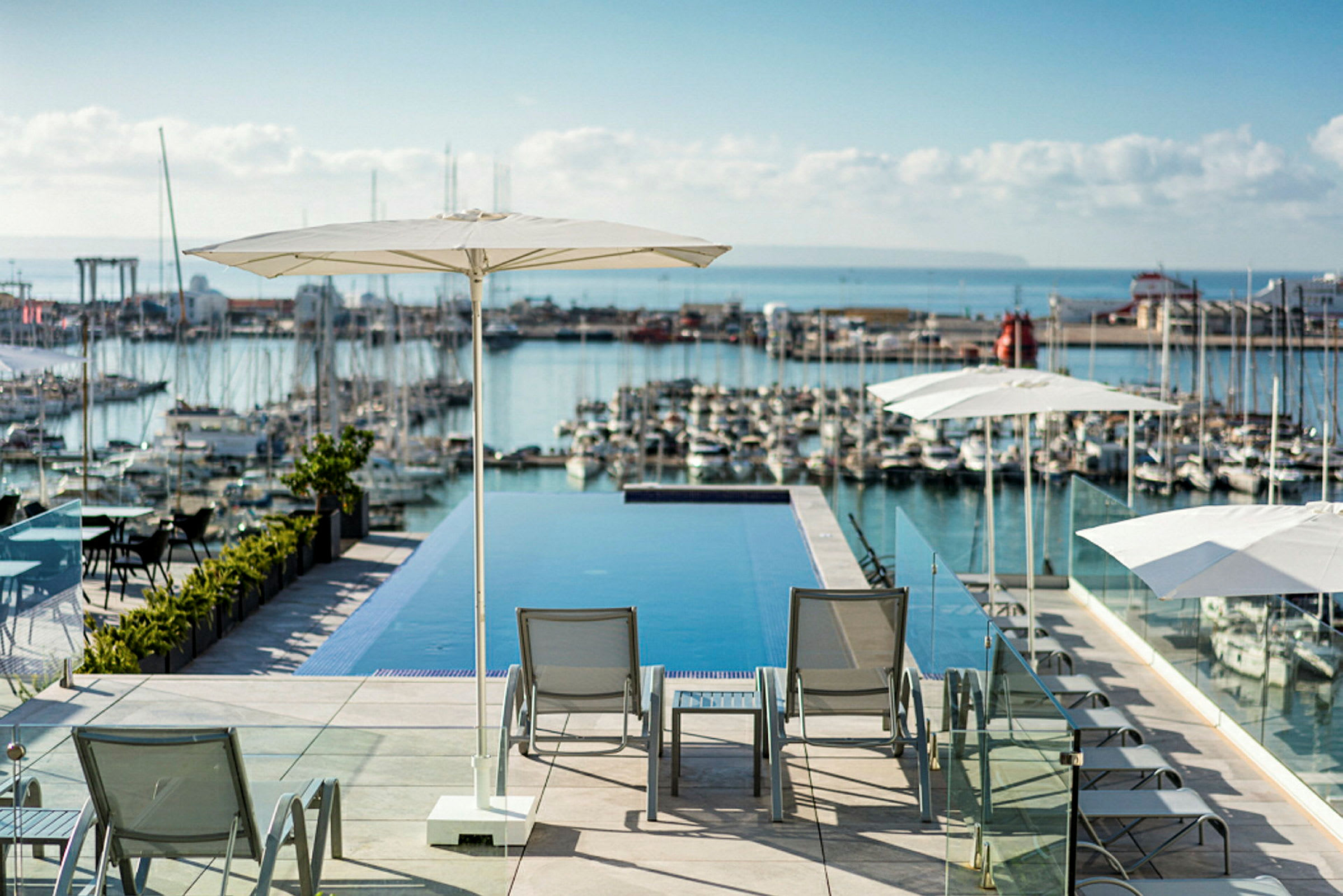 Bild av en infinitypool med vilstolar och parasoller i förgrunden och en småbåtshamn i bakgrunden. (AI-genererad text)