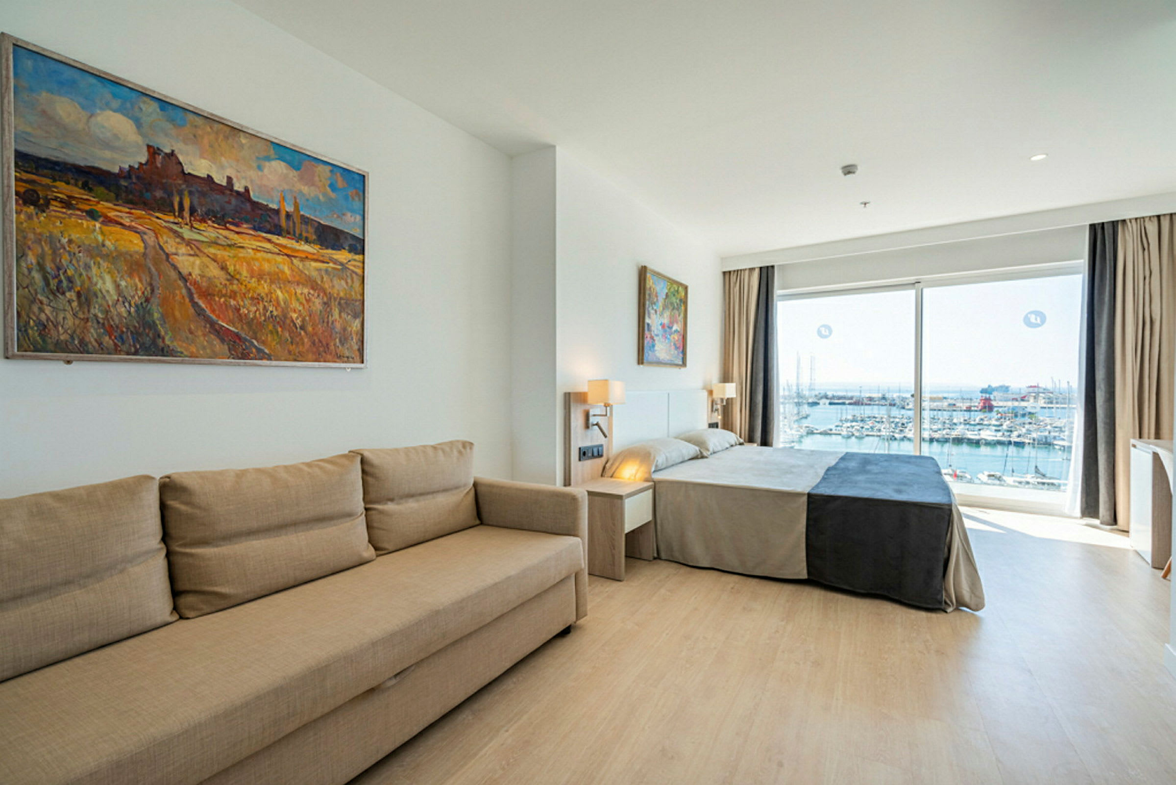 Ett hotellrum med en soffa, en säng och fönster som visar utsikt över en marina. (AI-genererad text)