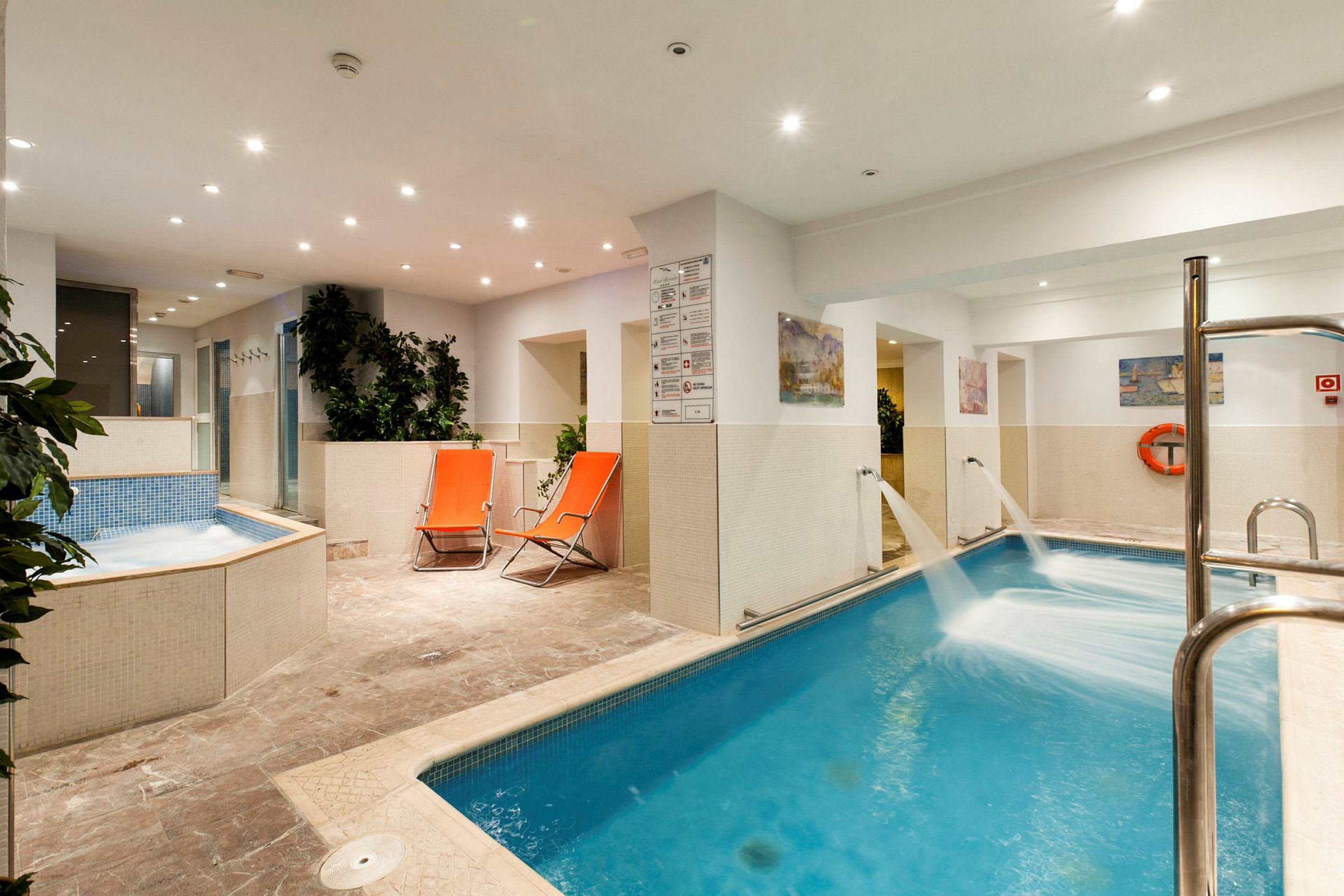 Inomhuspoolområde med bubbelpool, solsängar och gröna växter. (AI-genererad text)