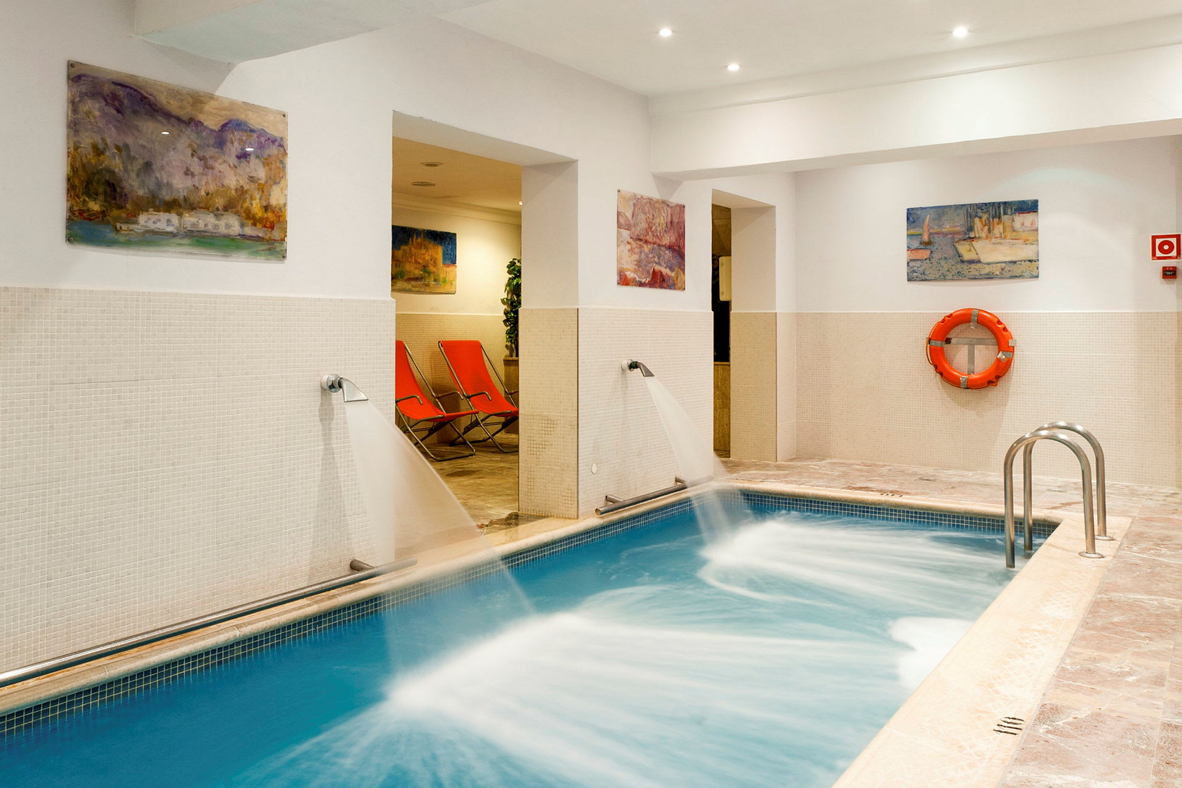 Inomhuspool med vattenstrålar och orangea solstolar i bakgrunden. (AI-genererad text)