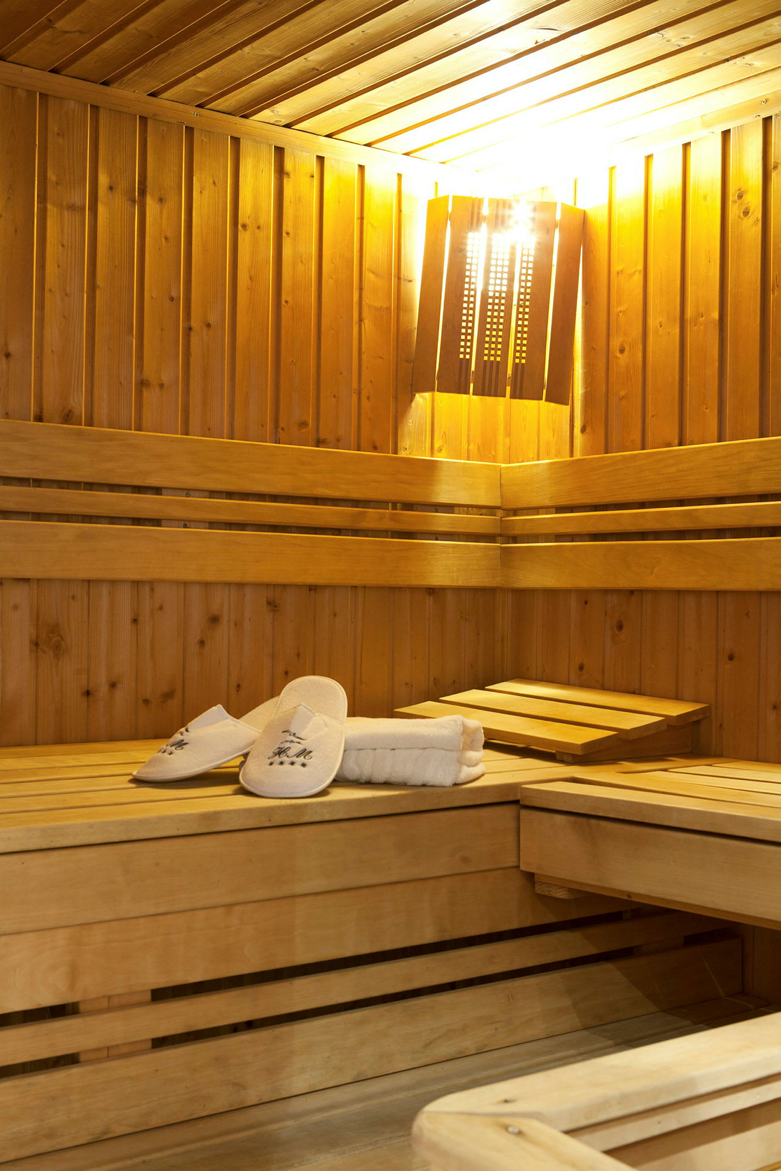 Ett träinrett basturum med bänkar och en mjukt ljussatt lampa. På en bänk ligger vita sandaler och handdukar. (AI-genererad text)