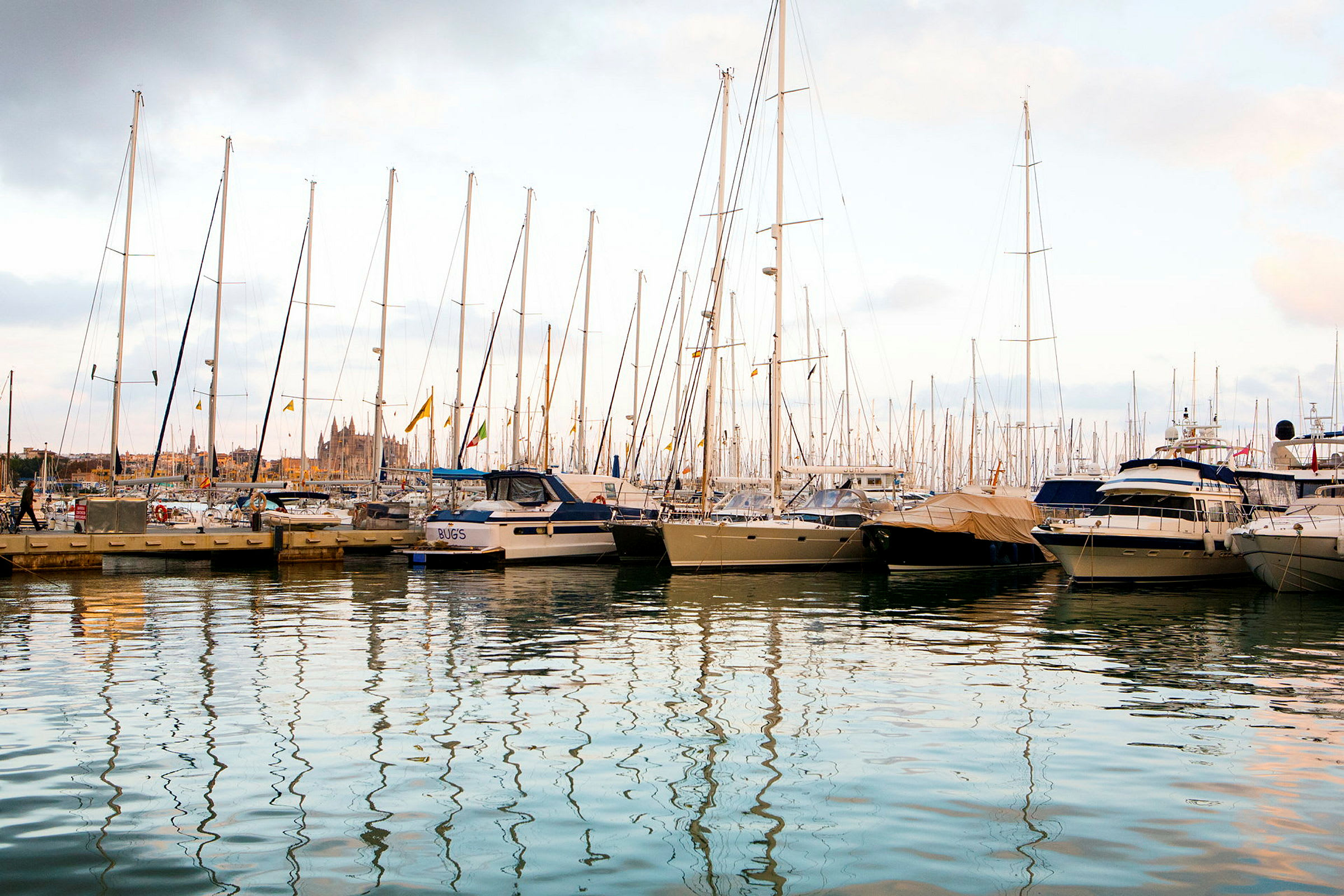 En hamn med många segelbåtar och motorbåtar förtöjda vid bryggor. Vattnet speglar de höga mastarna. (AI-genererad text)